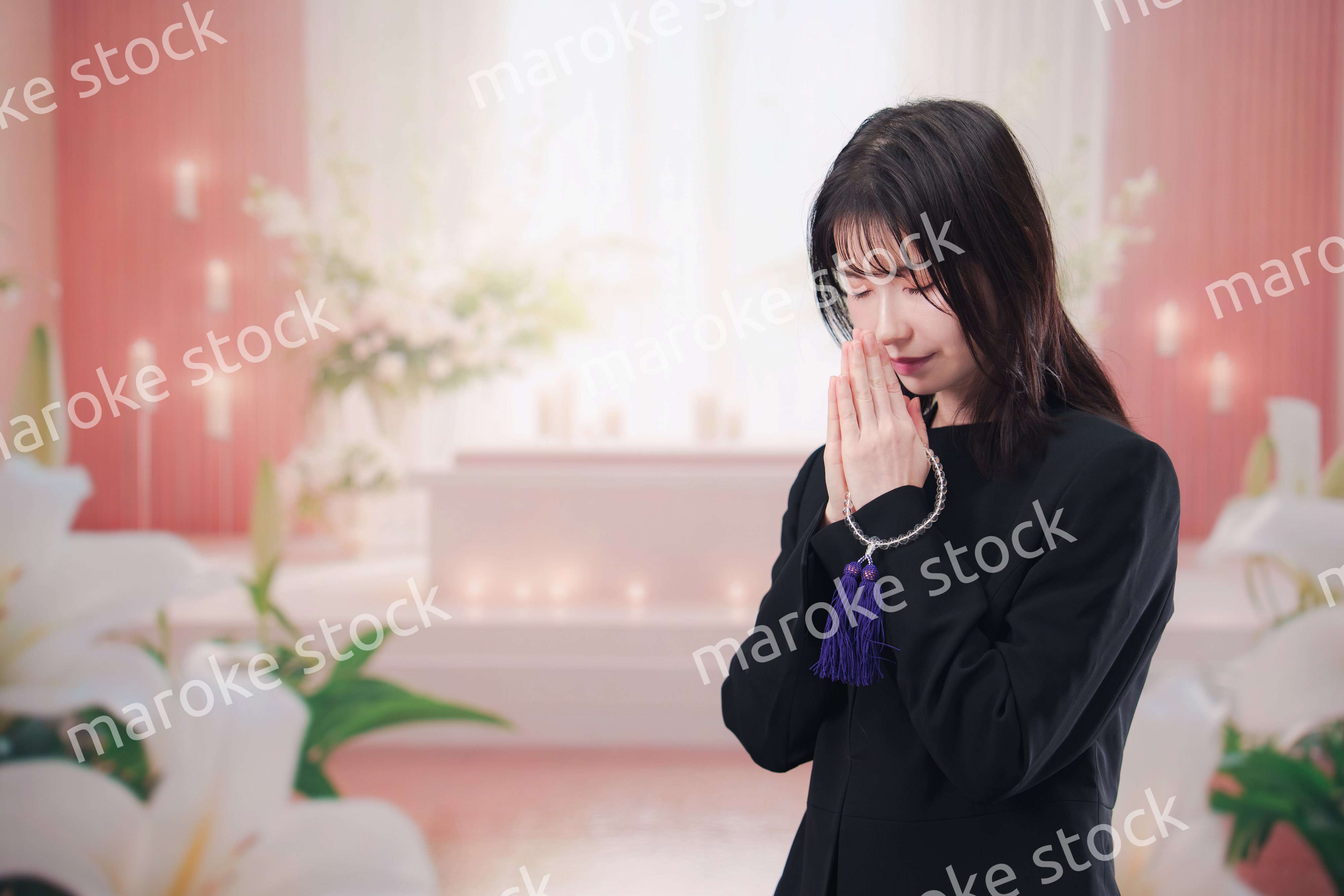 お葬式・お通夜で喪服を着て合掌をする若い女性