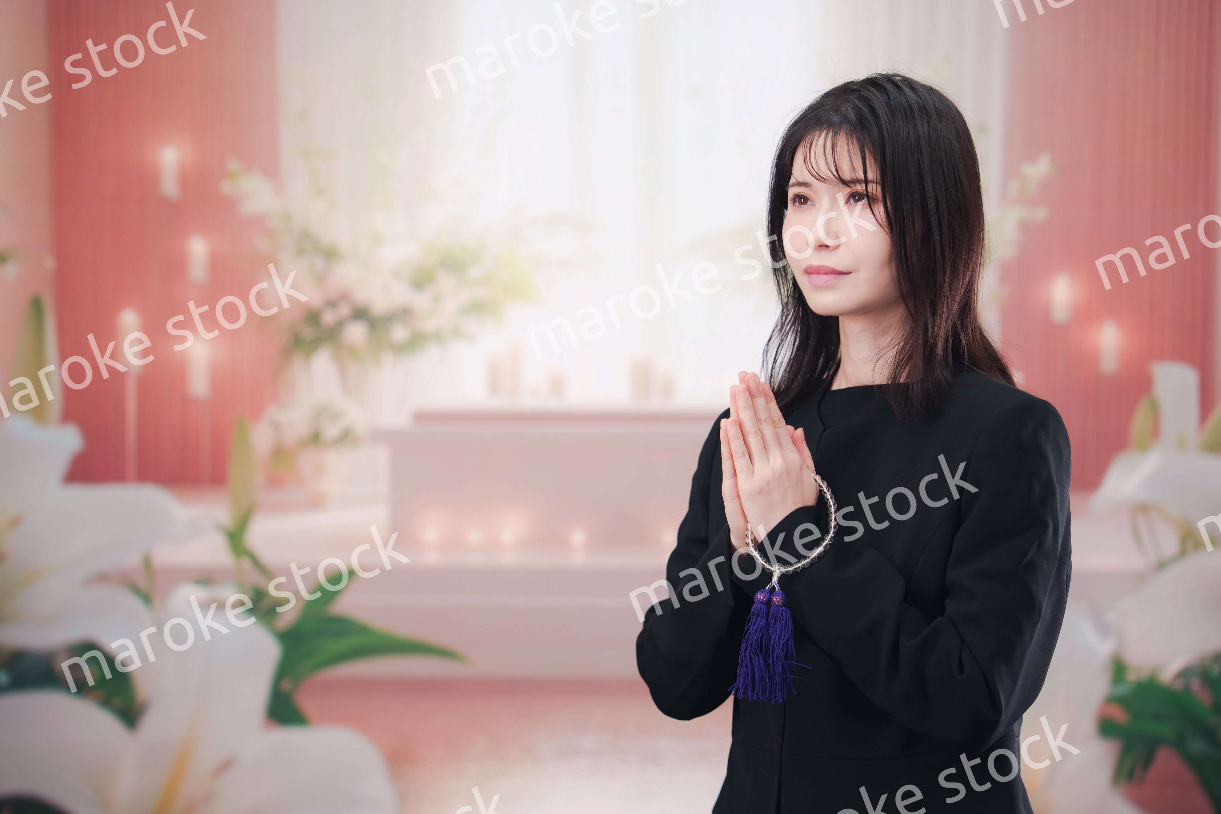 お葬式・お通夜で喪服を着て合掌をする若い女性