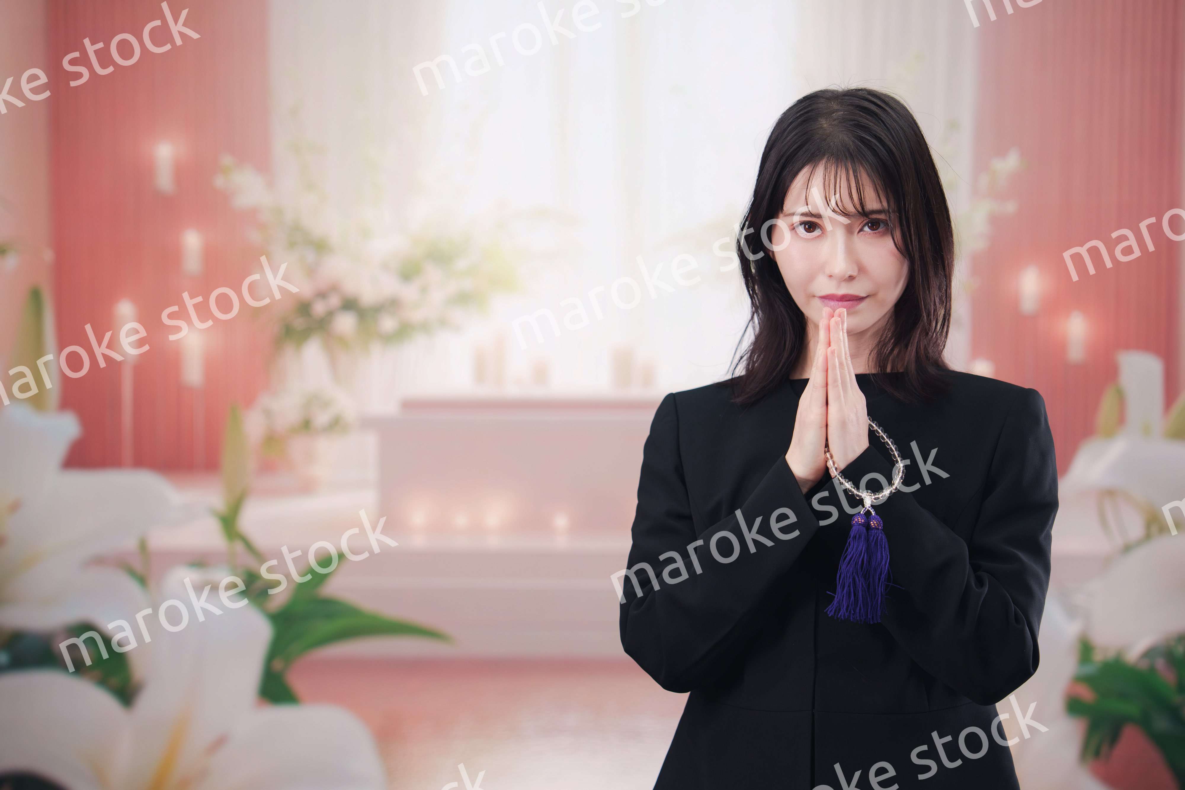 お葬式・お通夜で喪服を着て合掌をする若い女性