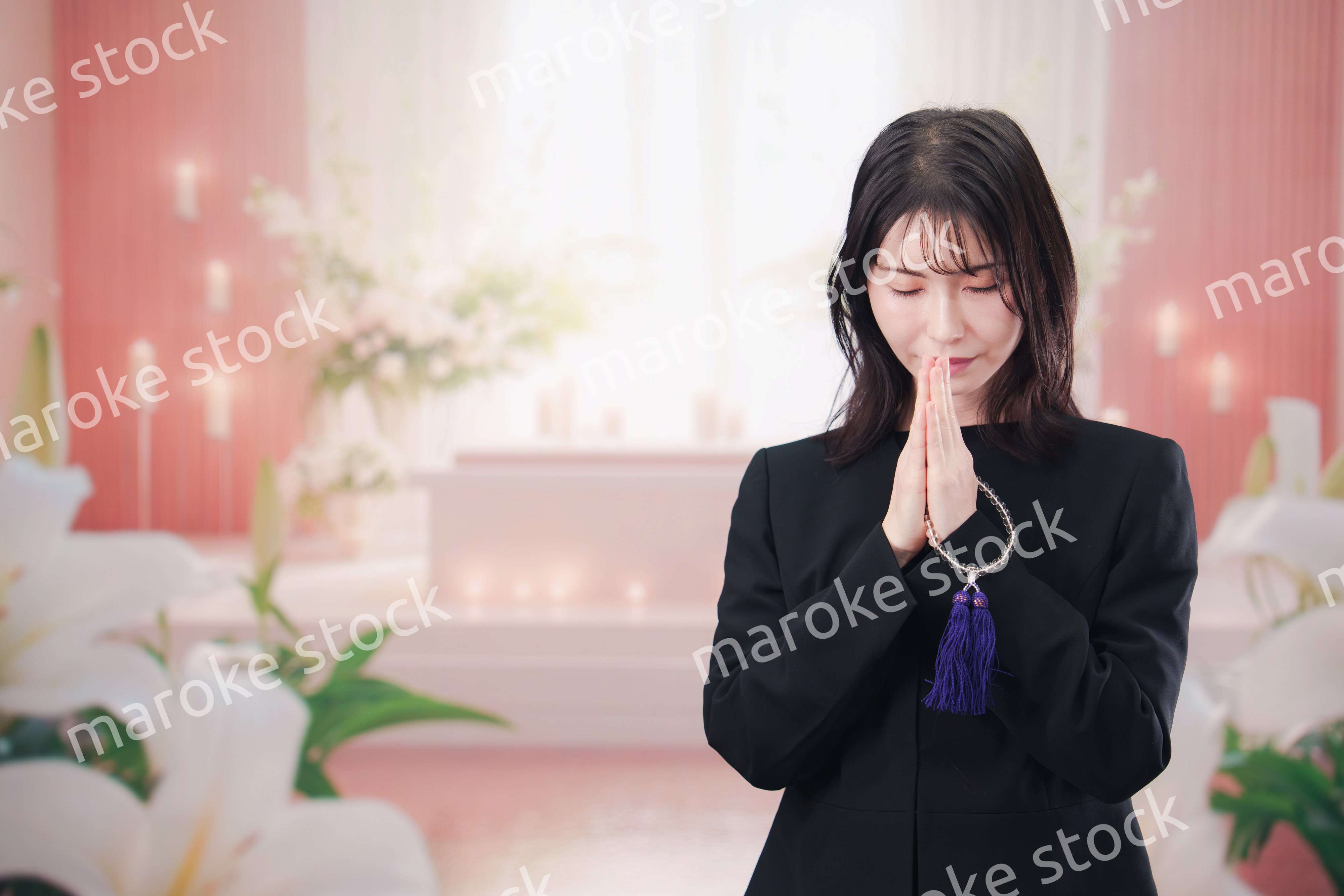 お葬式・お通夜で喪服を着て合掌をする若い女性