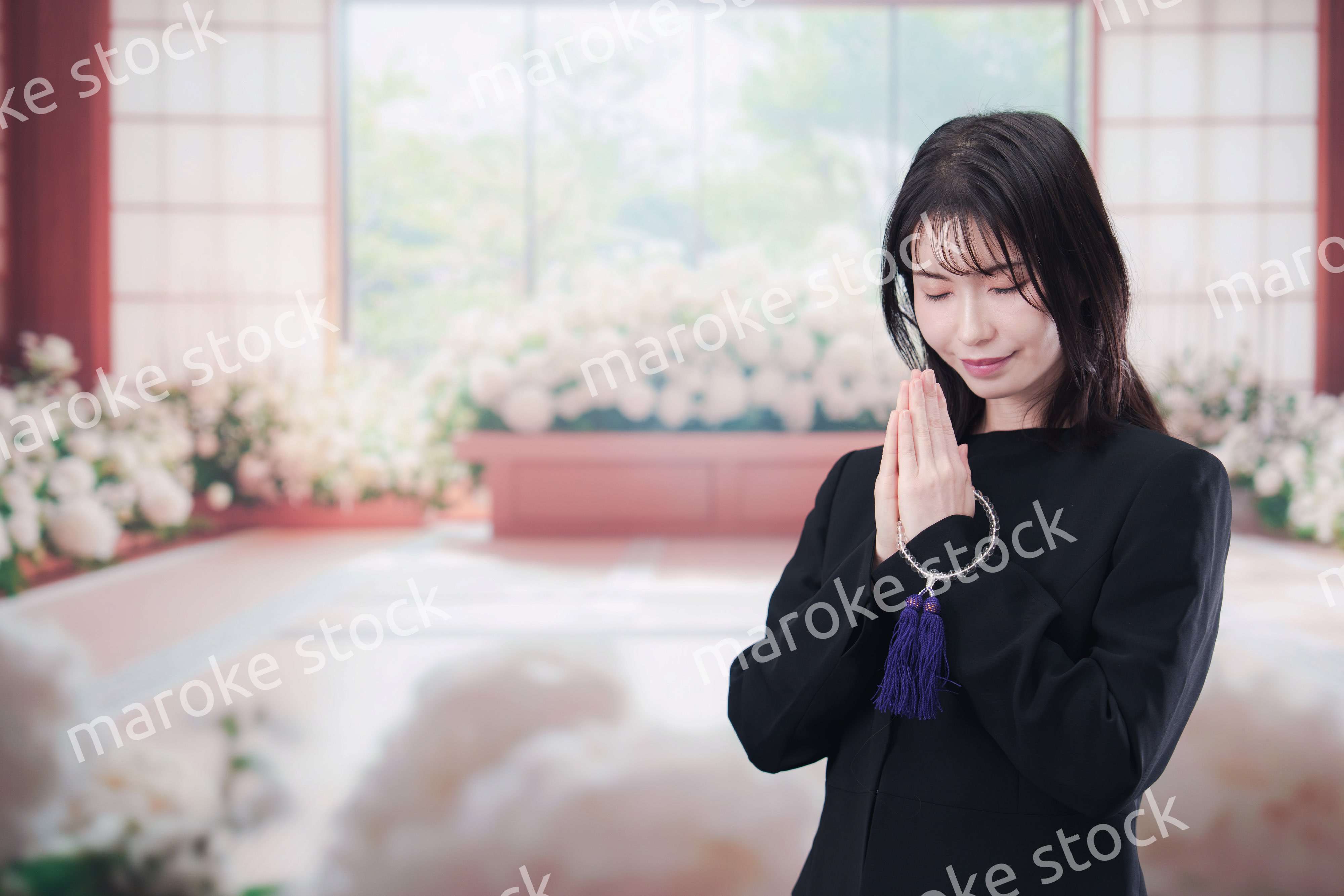 お葬式で合掌をする喪服を着た若い女性