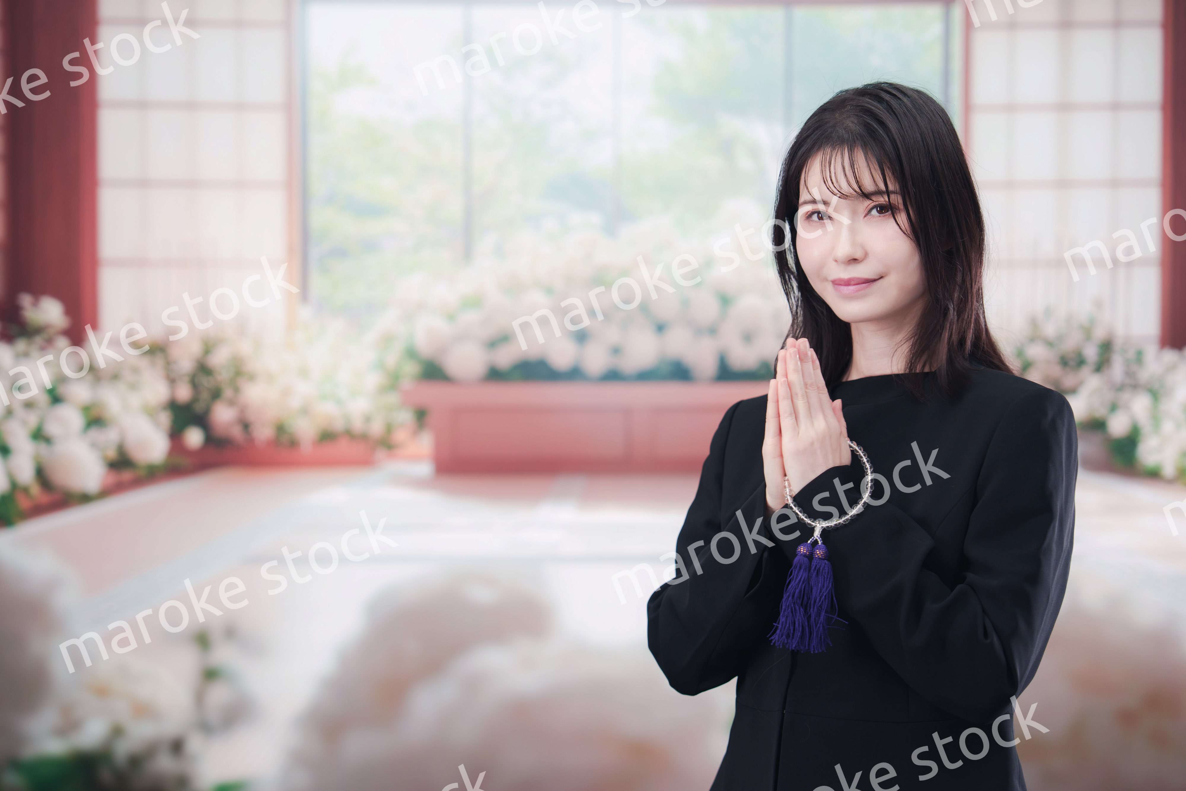 お葬式で合掌をする喪服を着た若い女性