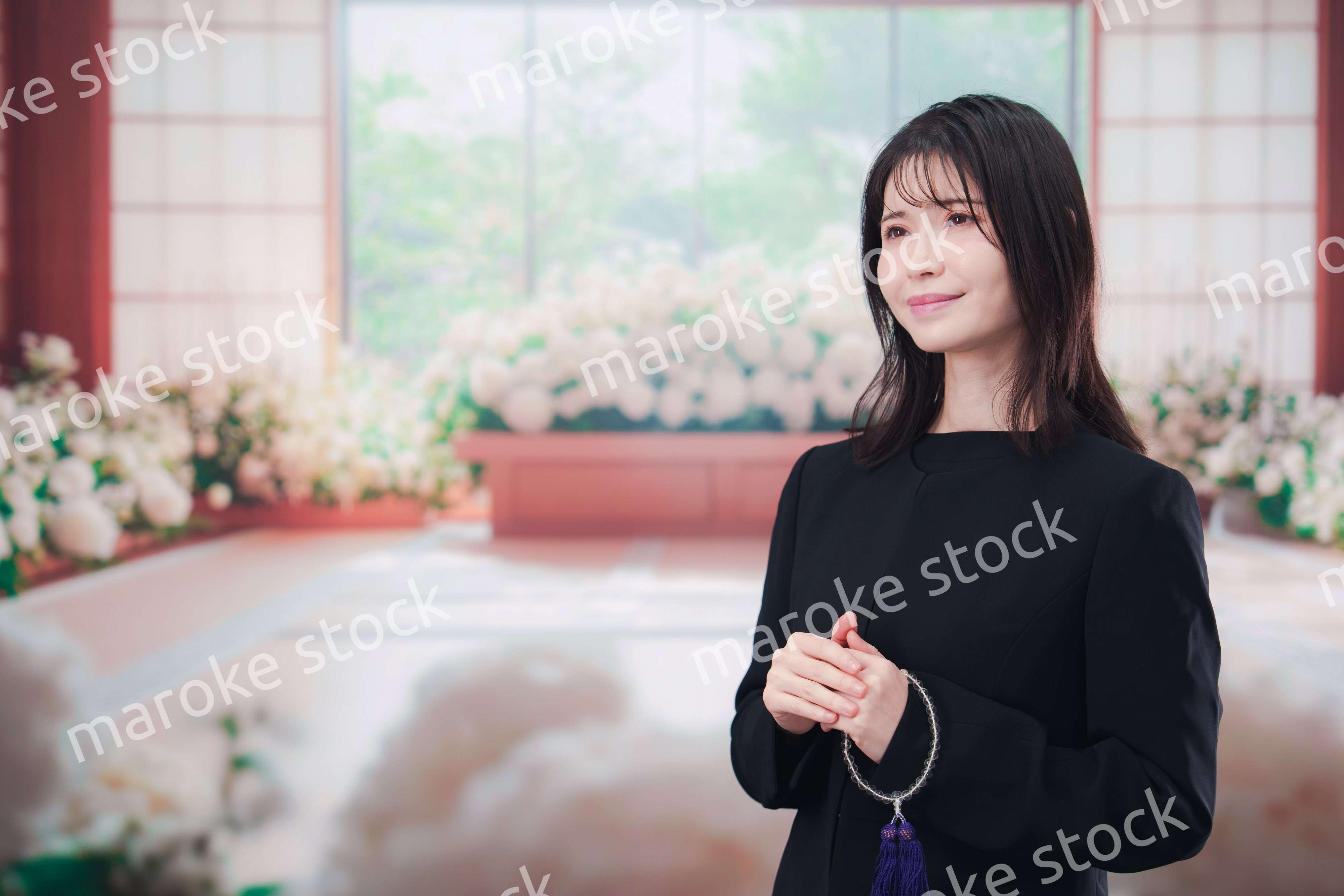 お葬式で喪服を着て数珠を持つ若い女性