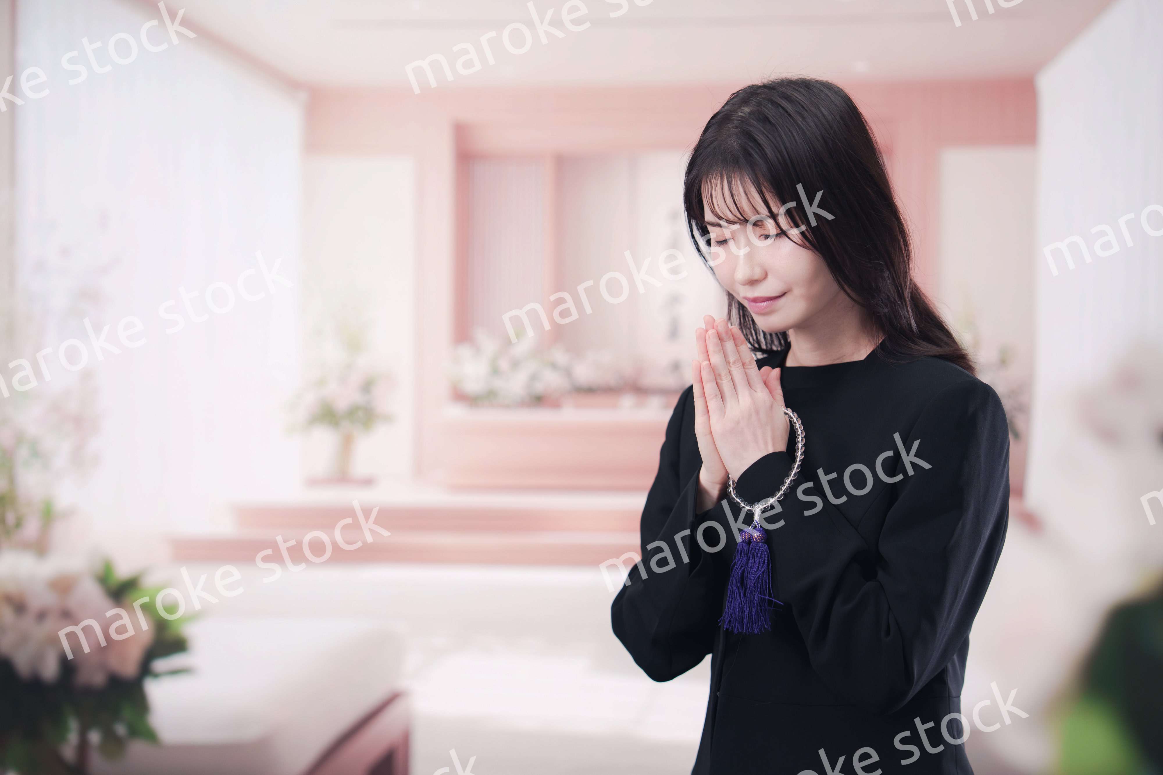 お葬式で合掌をする喪服を着た若い女性