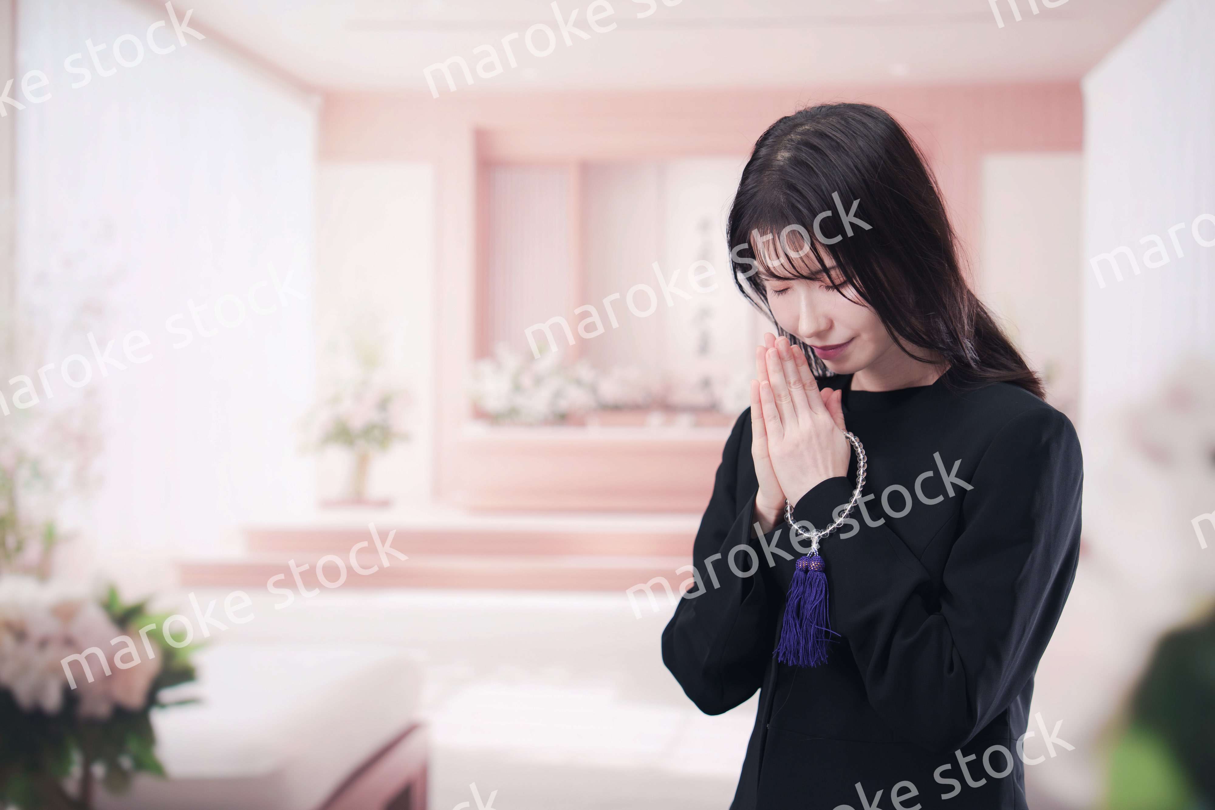 お葬式で合掌をする喪服を着た若い女性