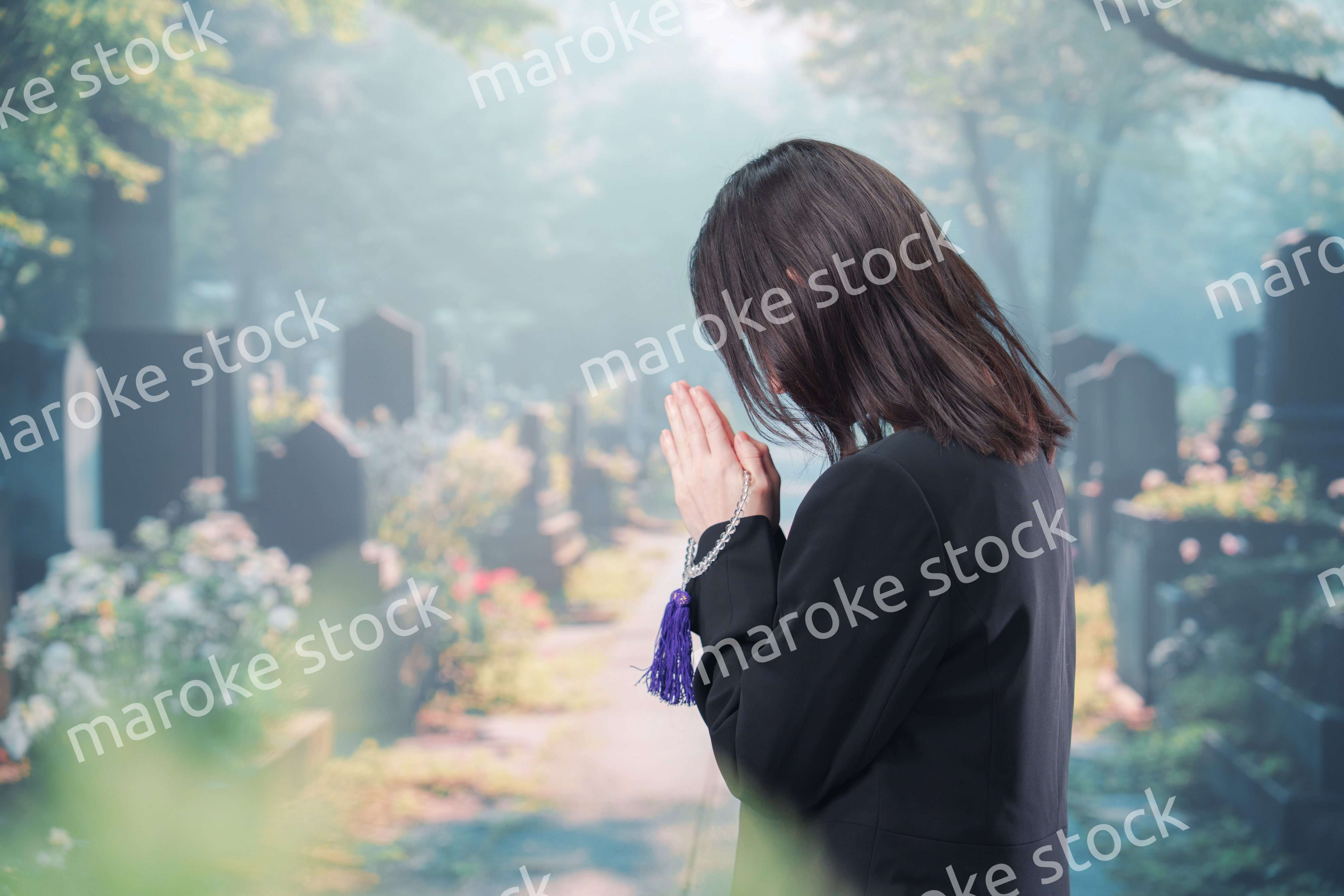 喪服を着て墓地で手を合わせる女性