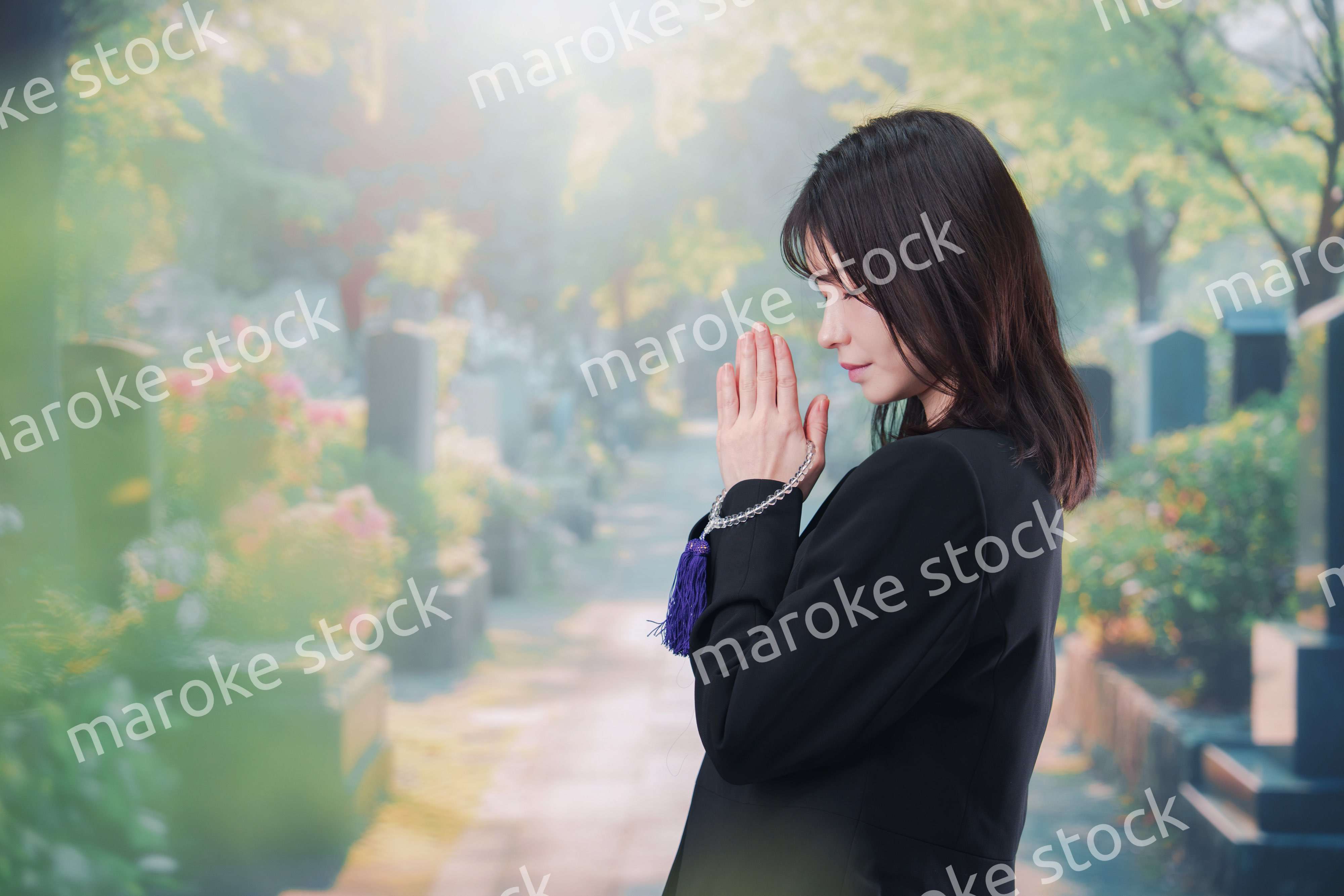 喪服を着て墓地で手を合わせる女性