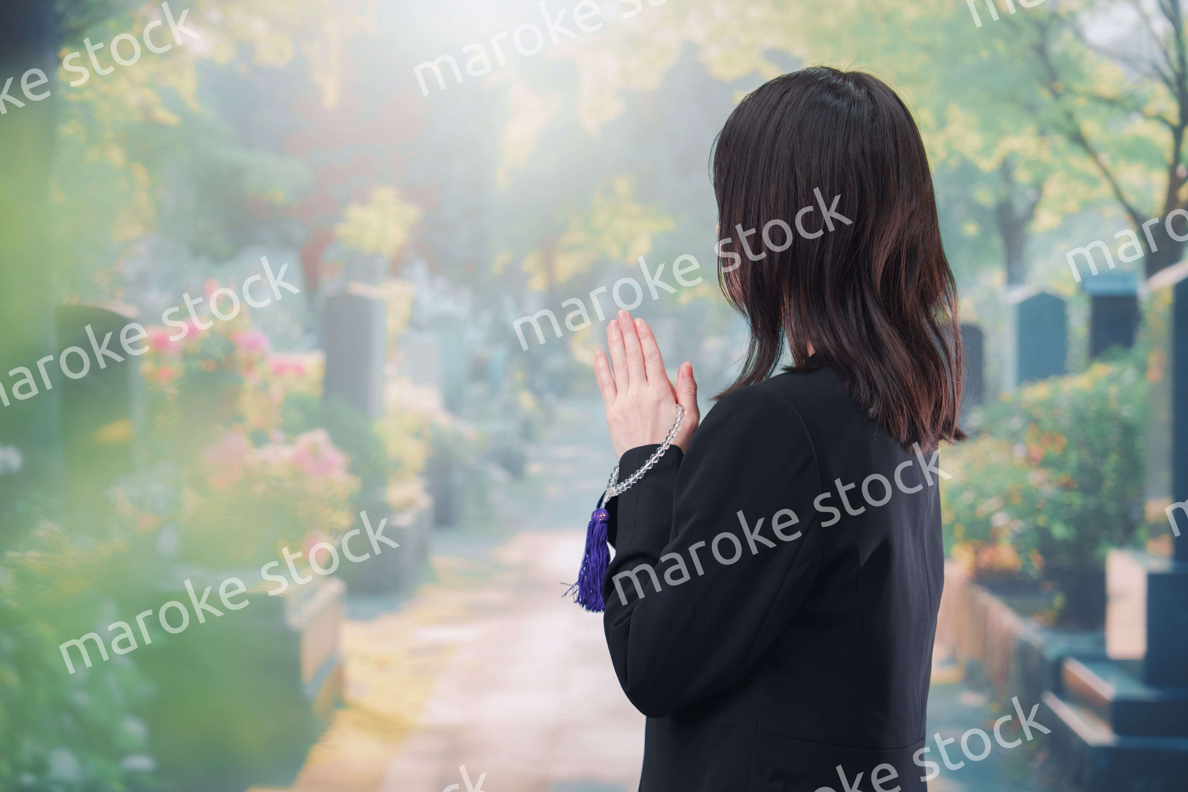 喪服を着て墓地で手を合わせる女性