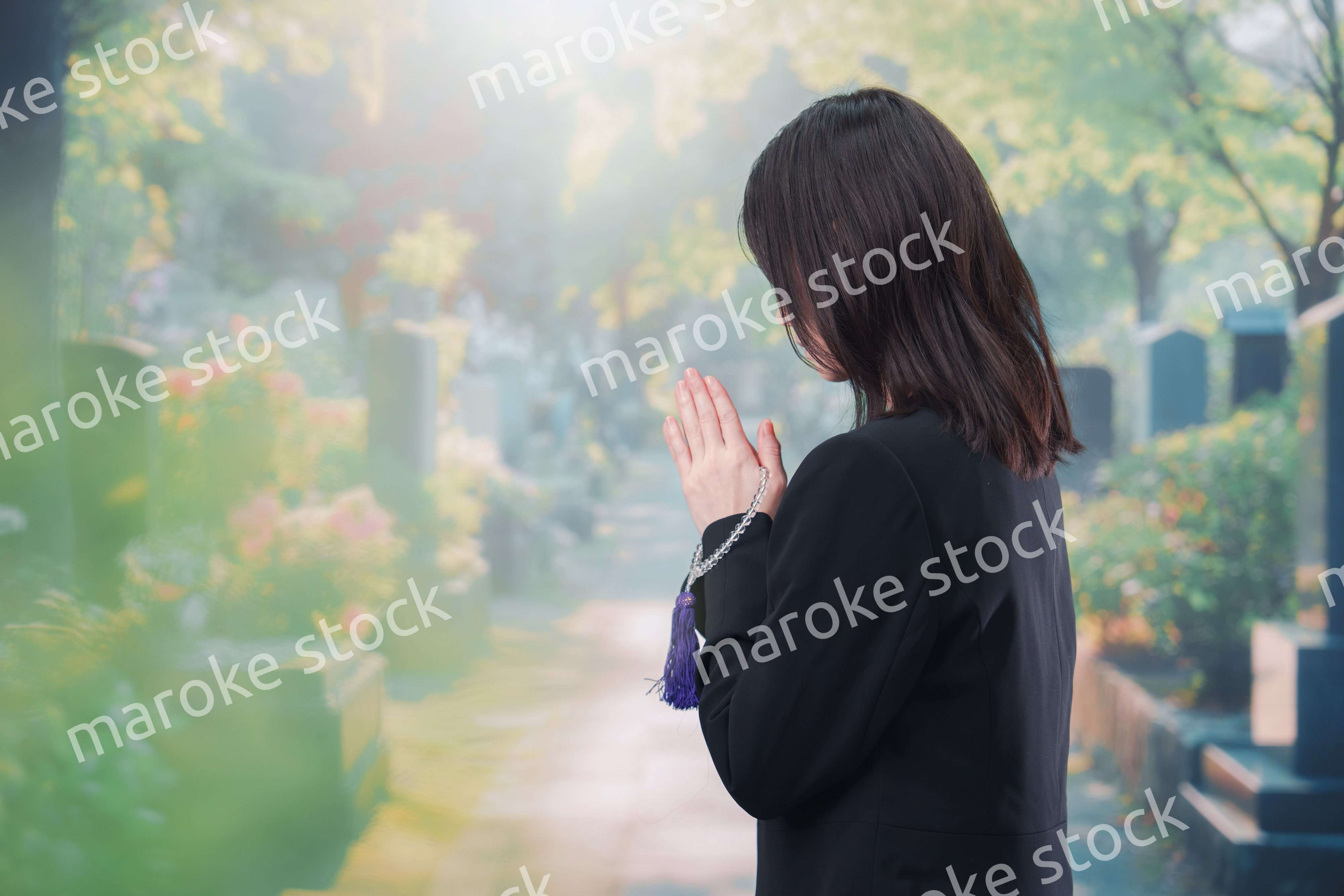 喪服を着て墓地で手を合わせる女性