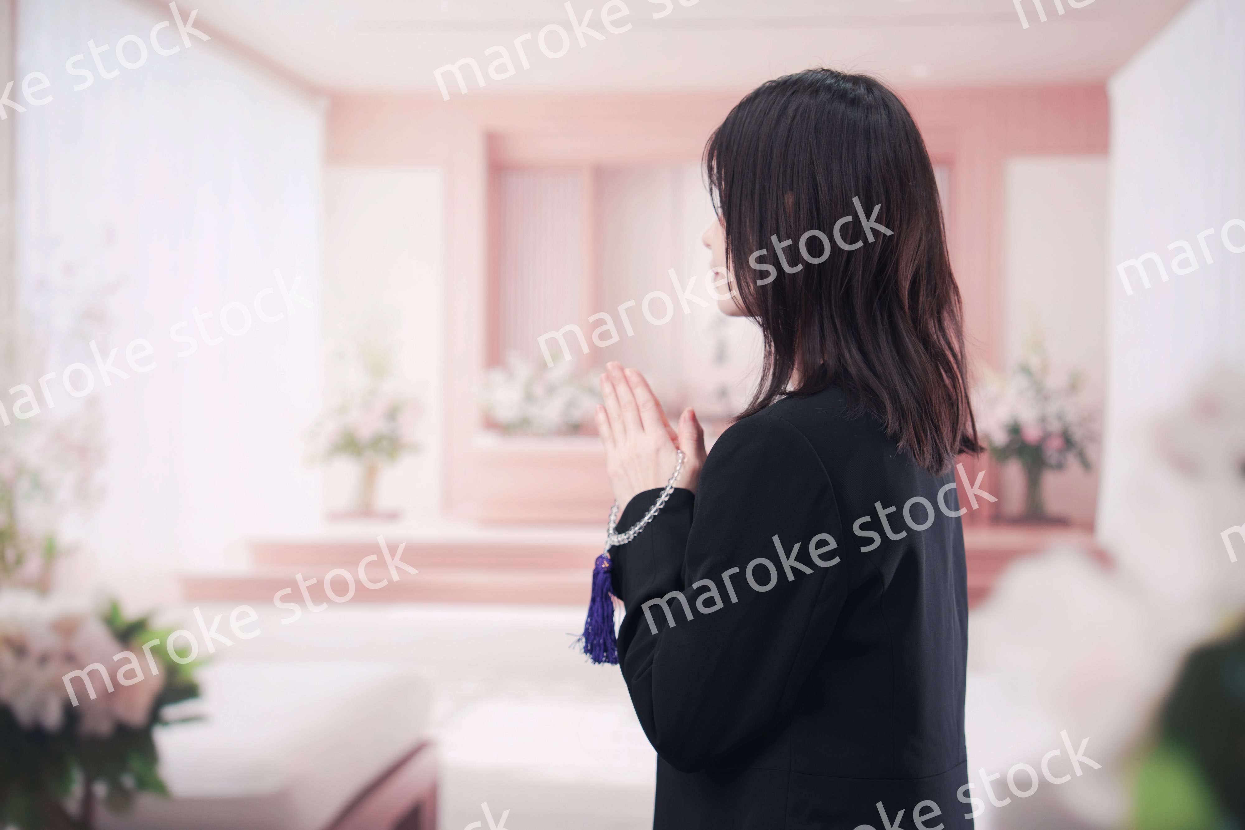 お葬式で合掌をする喪服を着た若い女性