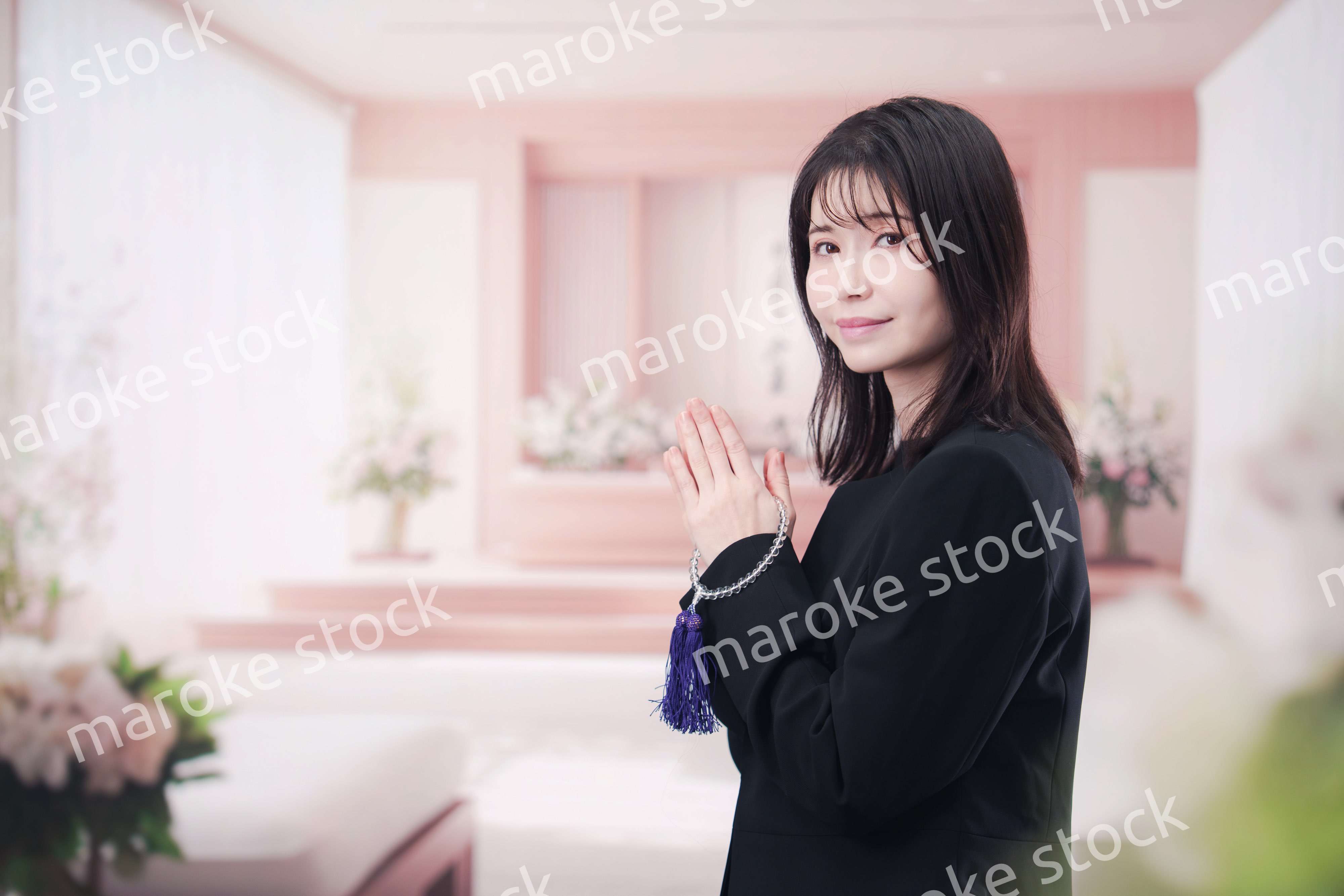 お葬式で合掌をする喪服を着た若い女性