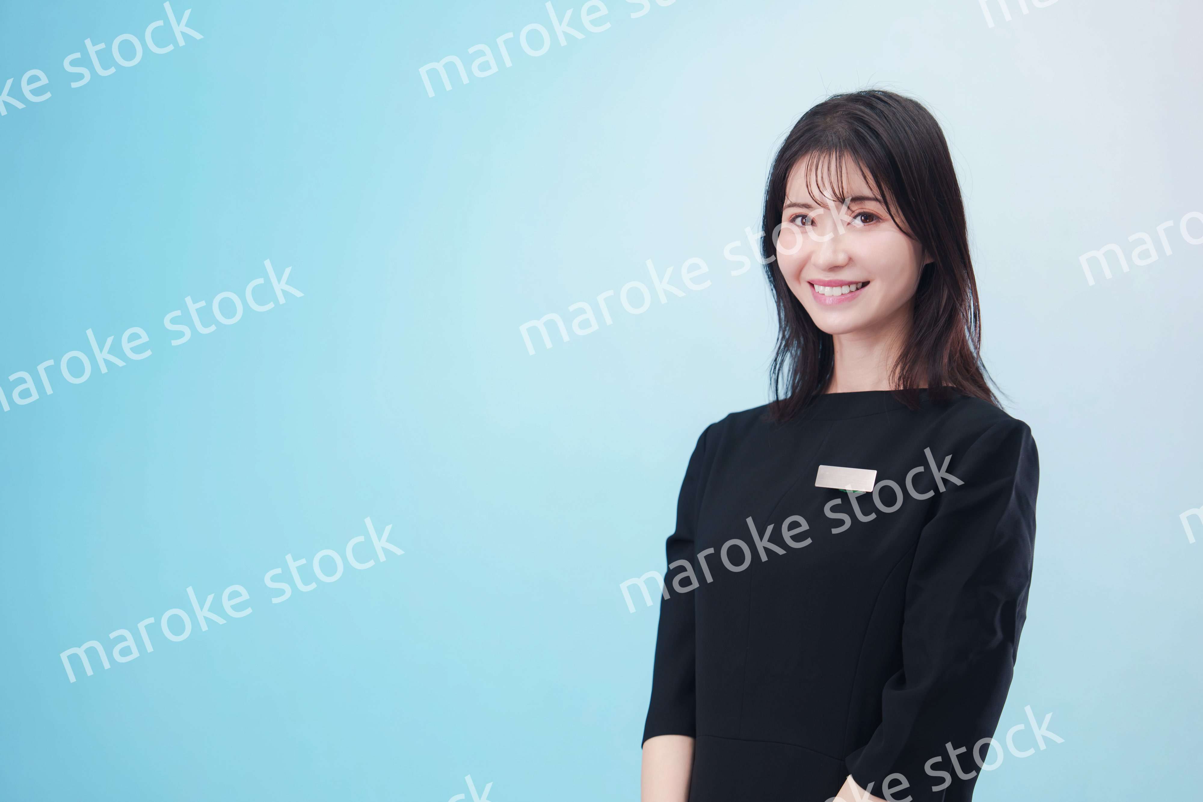 黒い服に名札をつけた笑顔のスタッフ（水色背景）