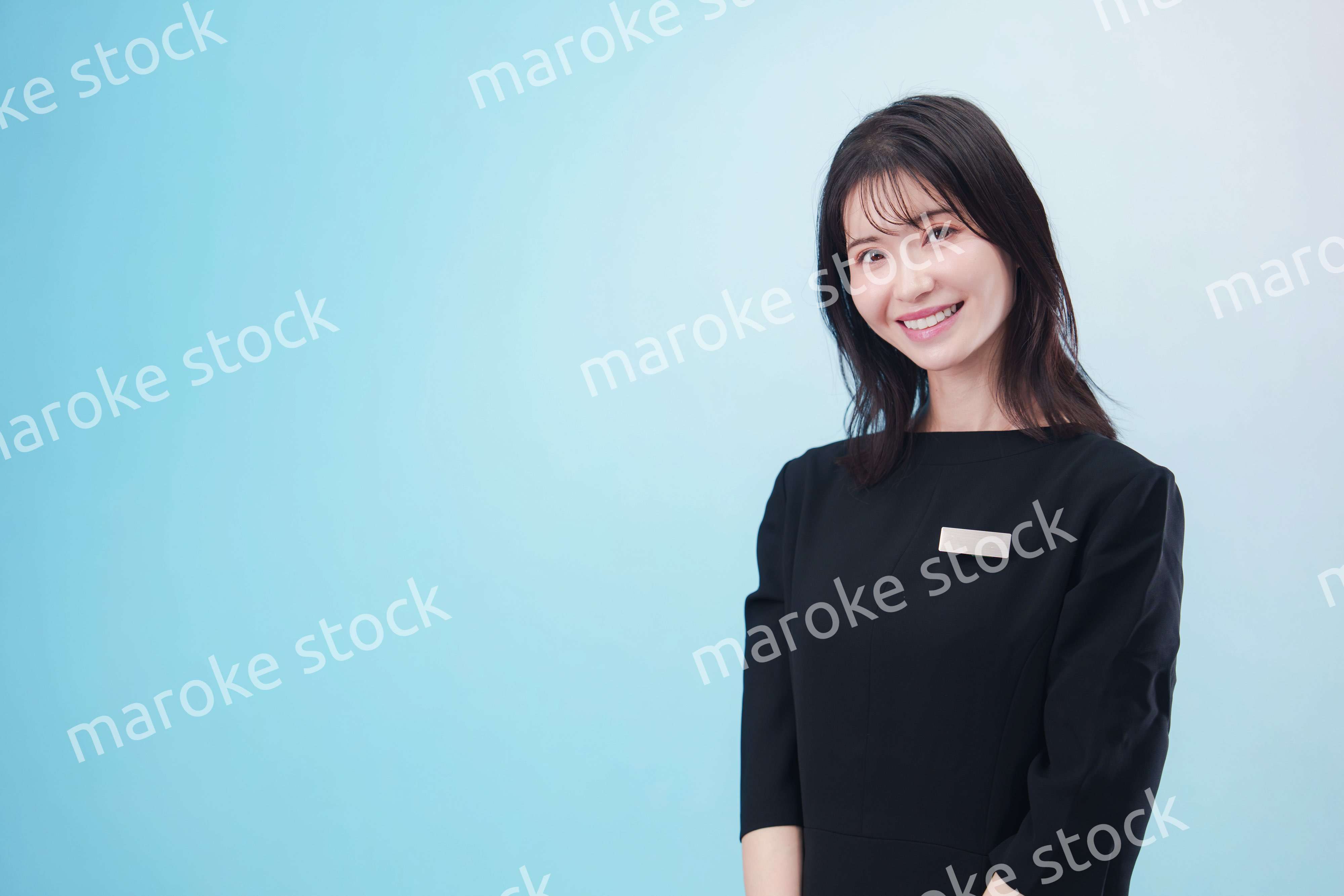 黒い服に名札をつけた笑顔のスタッフ（水色背景）