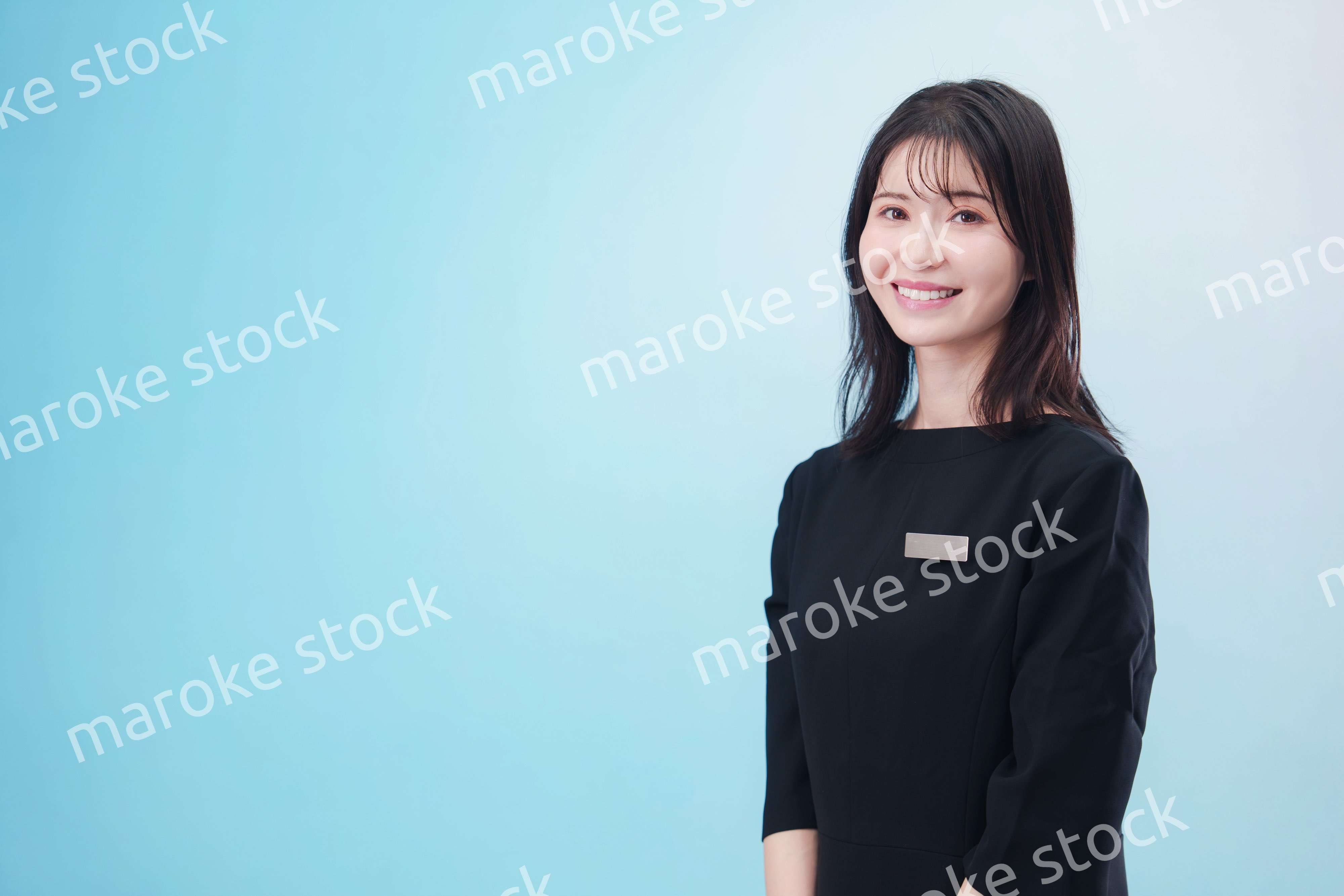 黒い服に名札をつけた笑顔のスタッフ（水色背景）