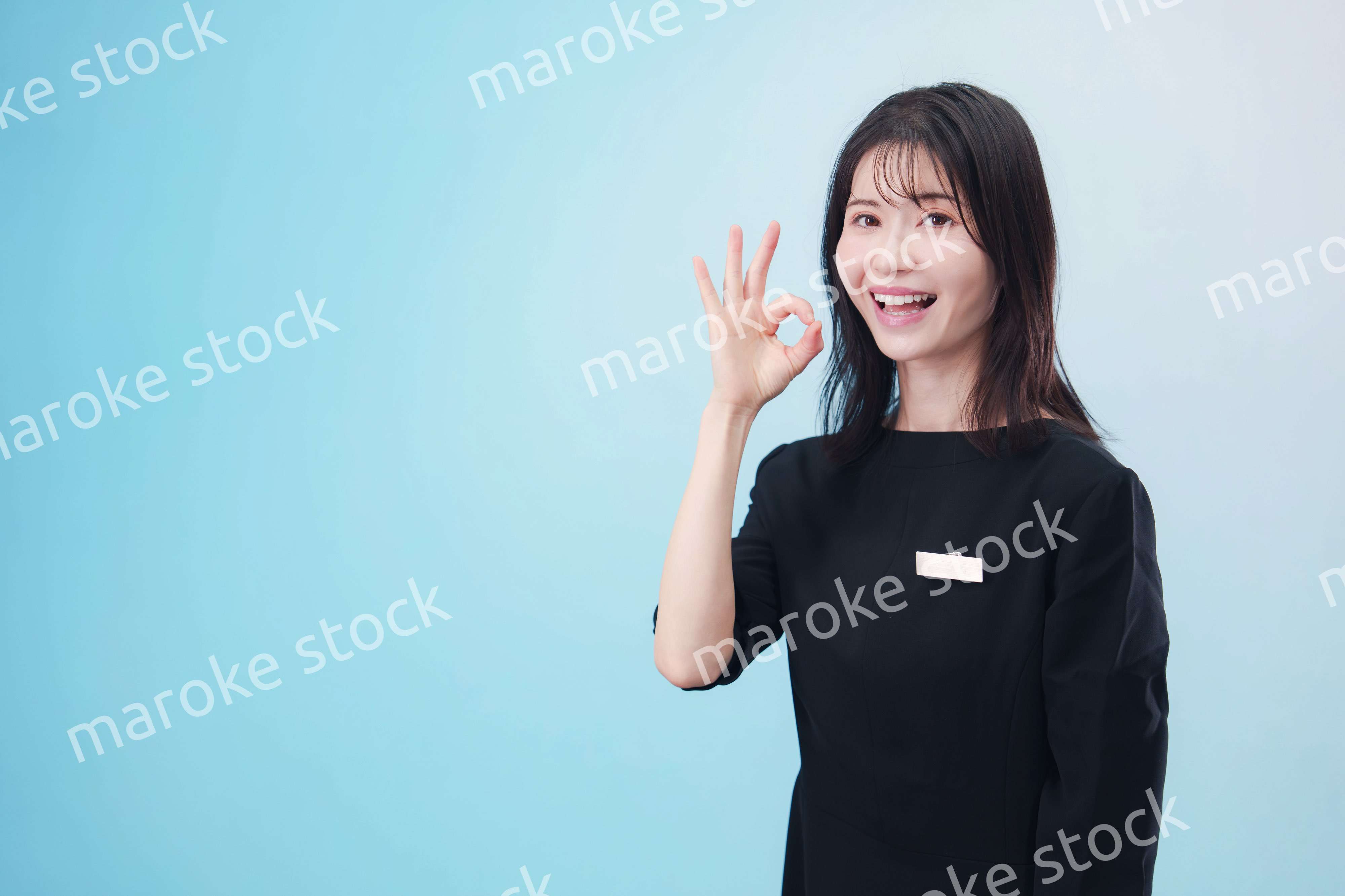 黒い服に名札をつけた笑顔のスタッフ（水色背景）