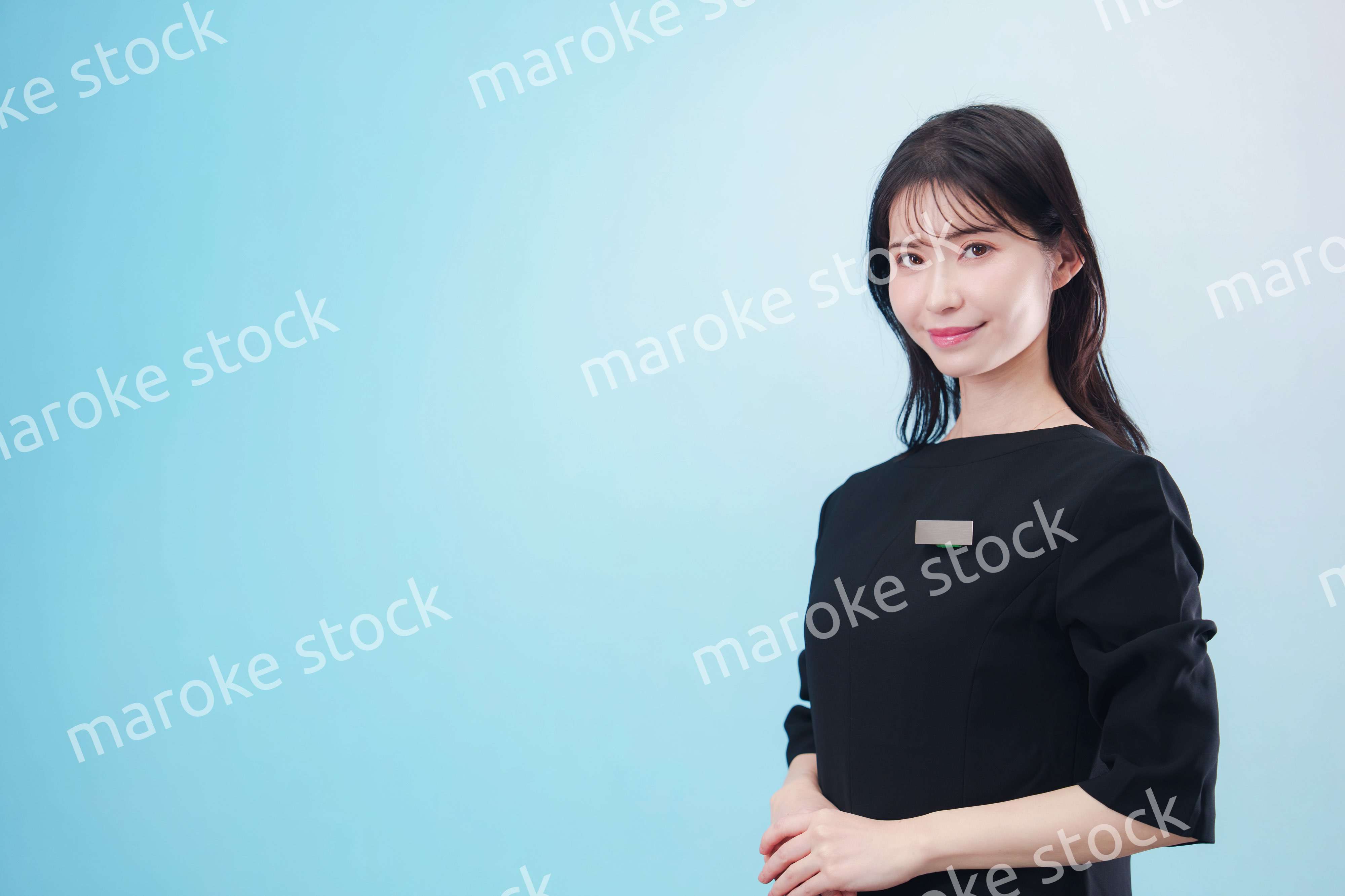 黒い服に名札をつけた笑顔のスタッフ（水色背景）