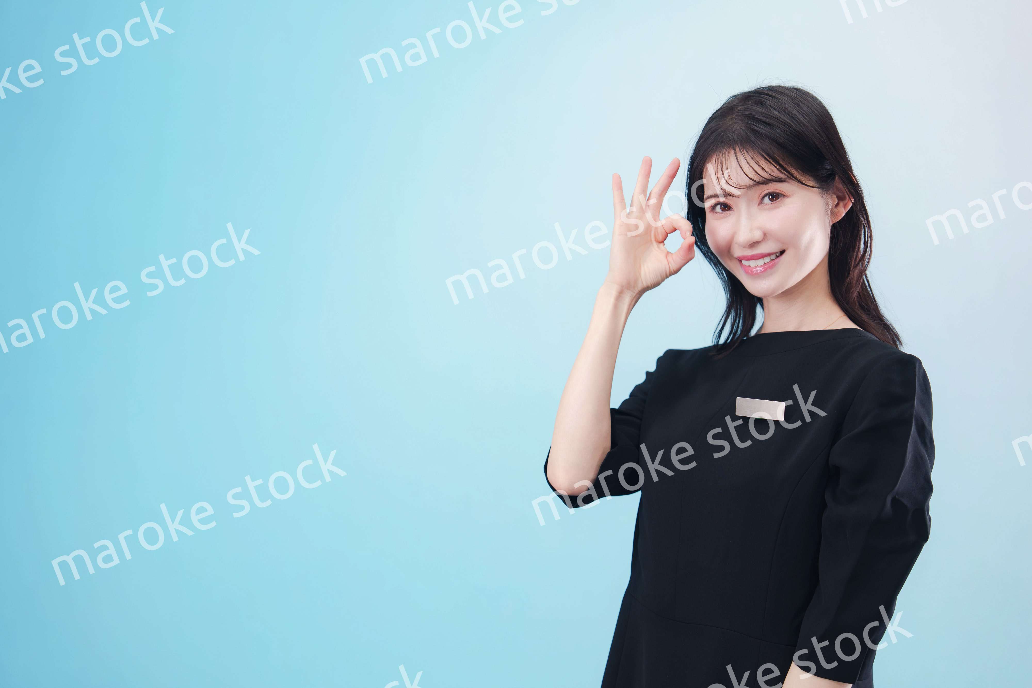 黒い服に名札をつけた笑顔のスタッフ（水色背景）