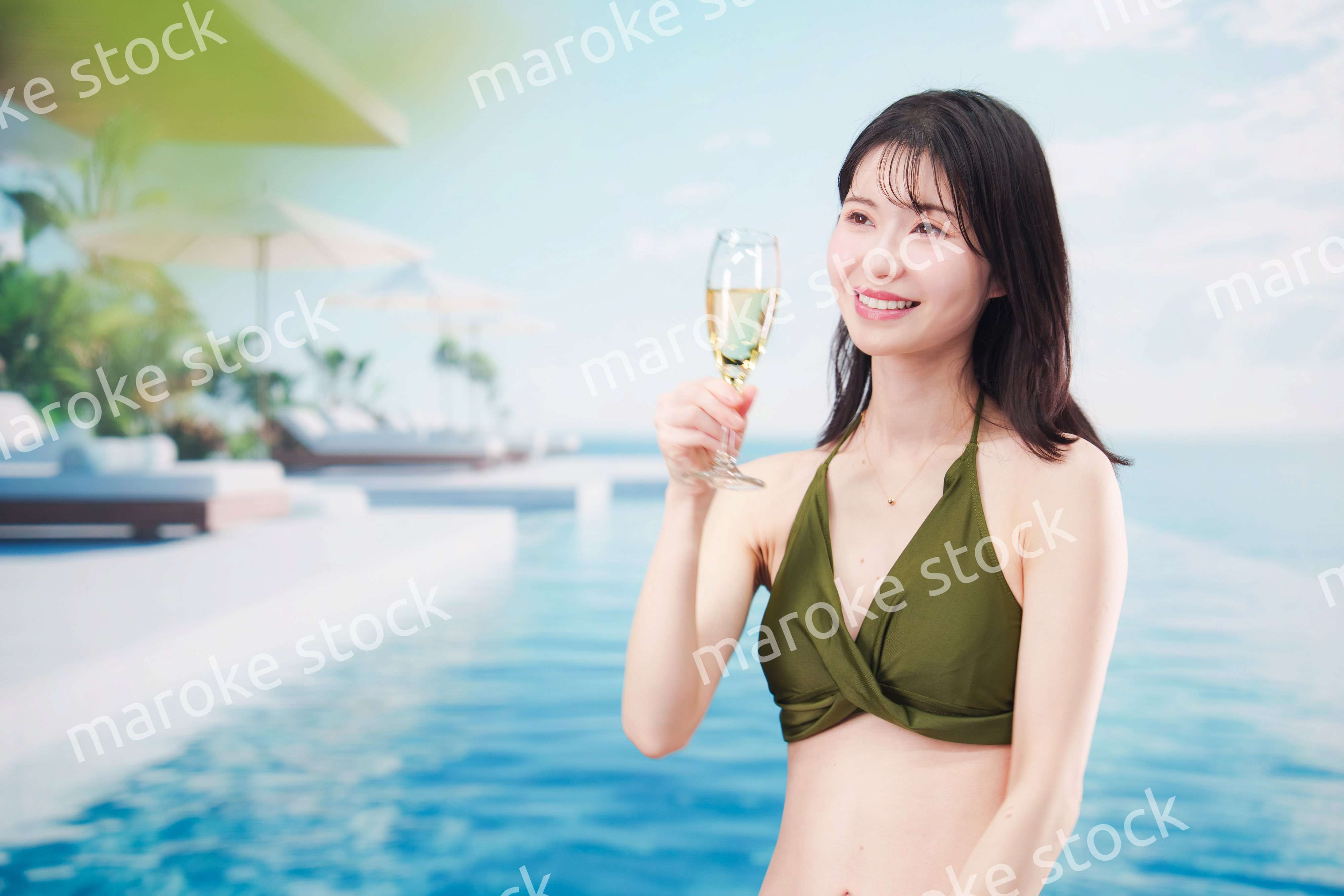 リゾートのプールで水着を着てスパークリングワインを飲む若い女性