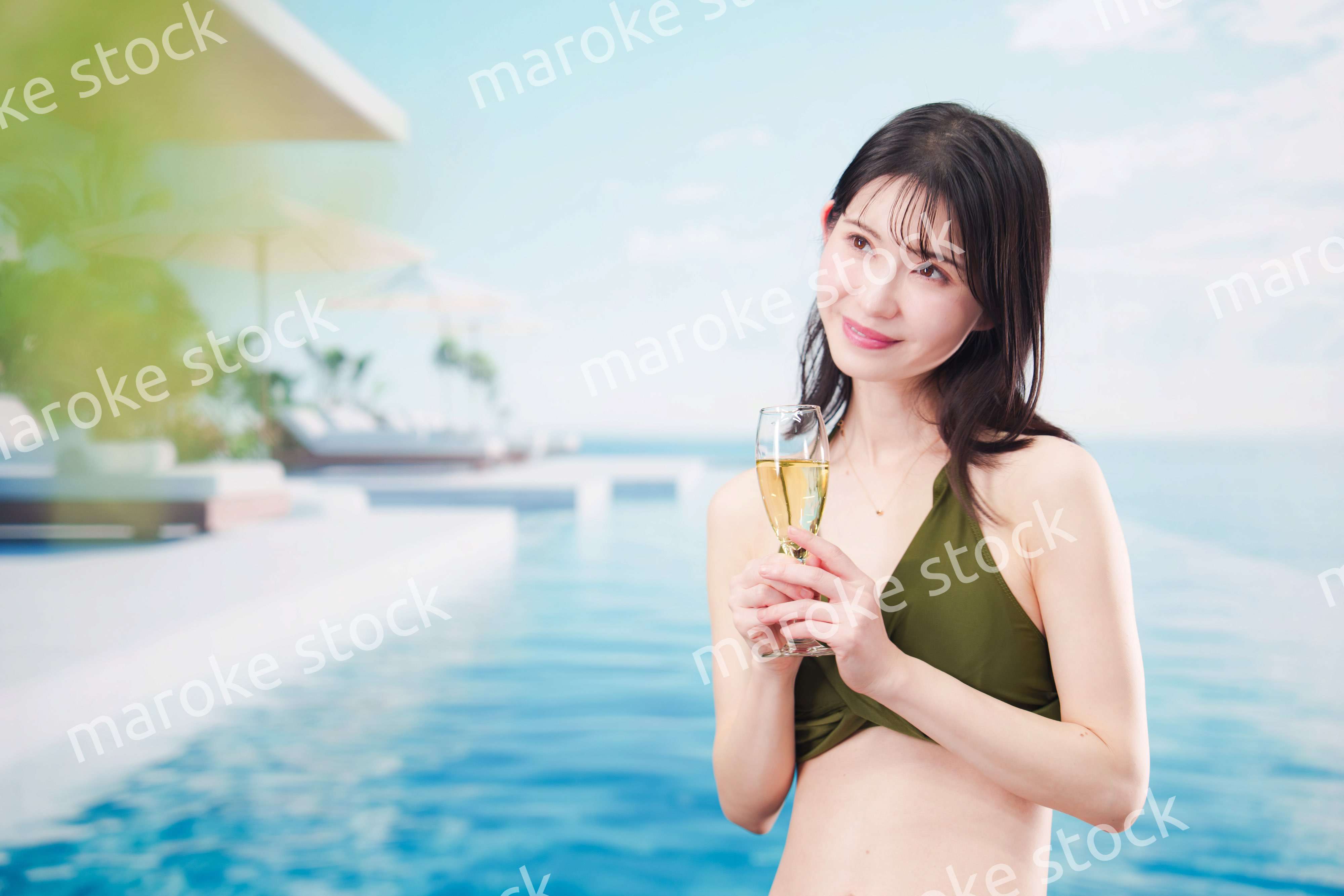 リゾートのプールで水着を着てスパークリングワインを飲む若い女性