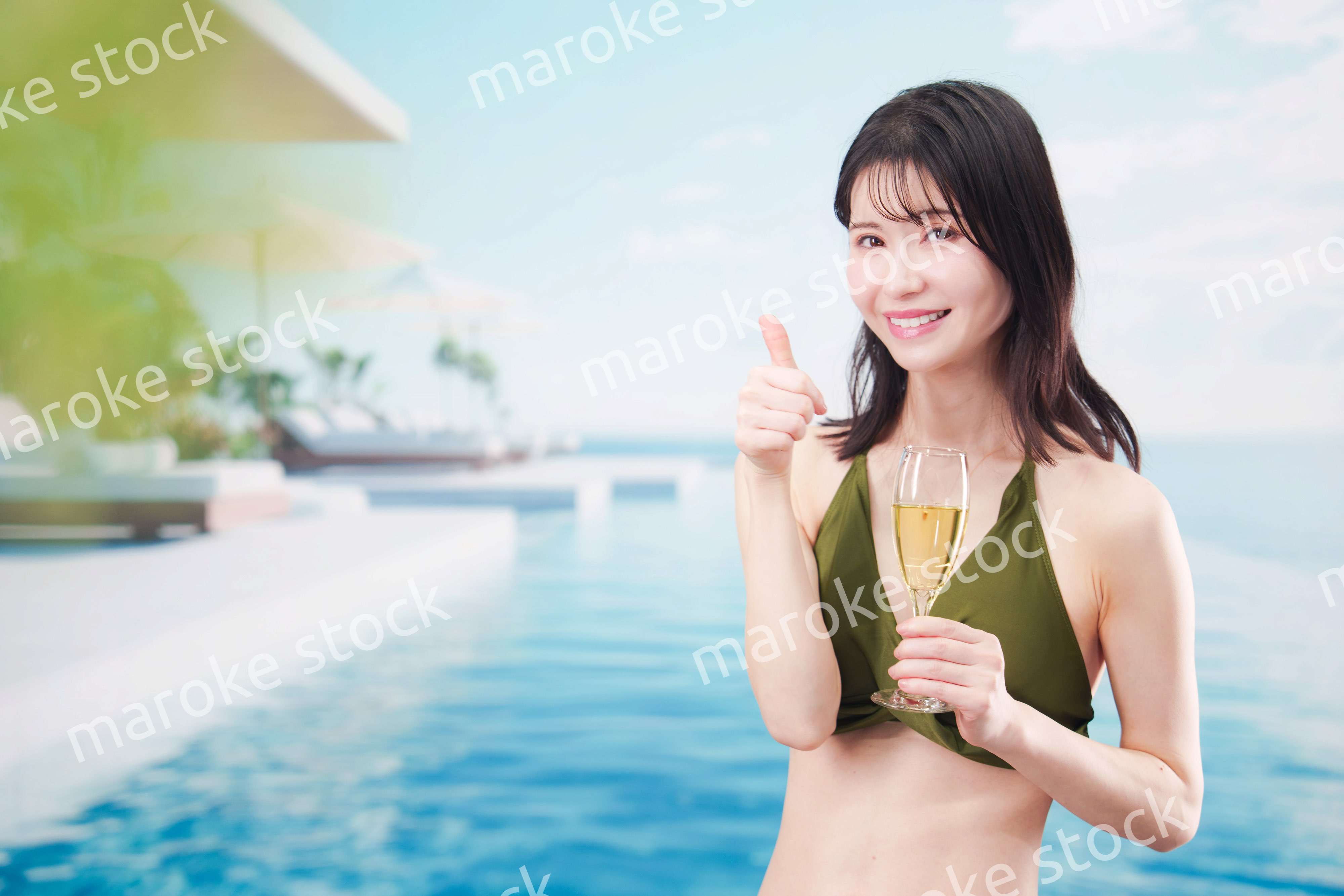 リゾートのプールで水着を着てスパークリングワインを飲む若い女性