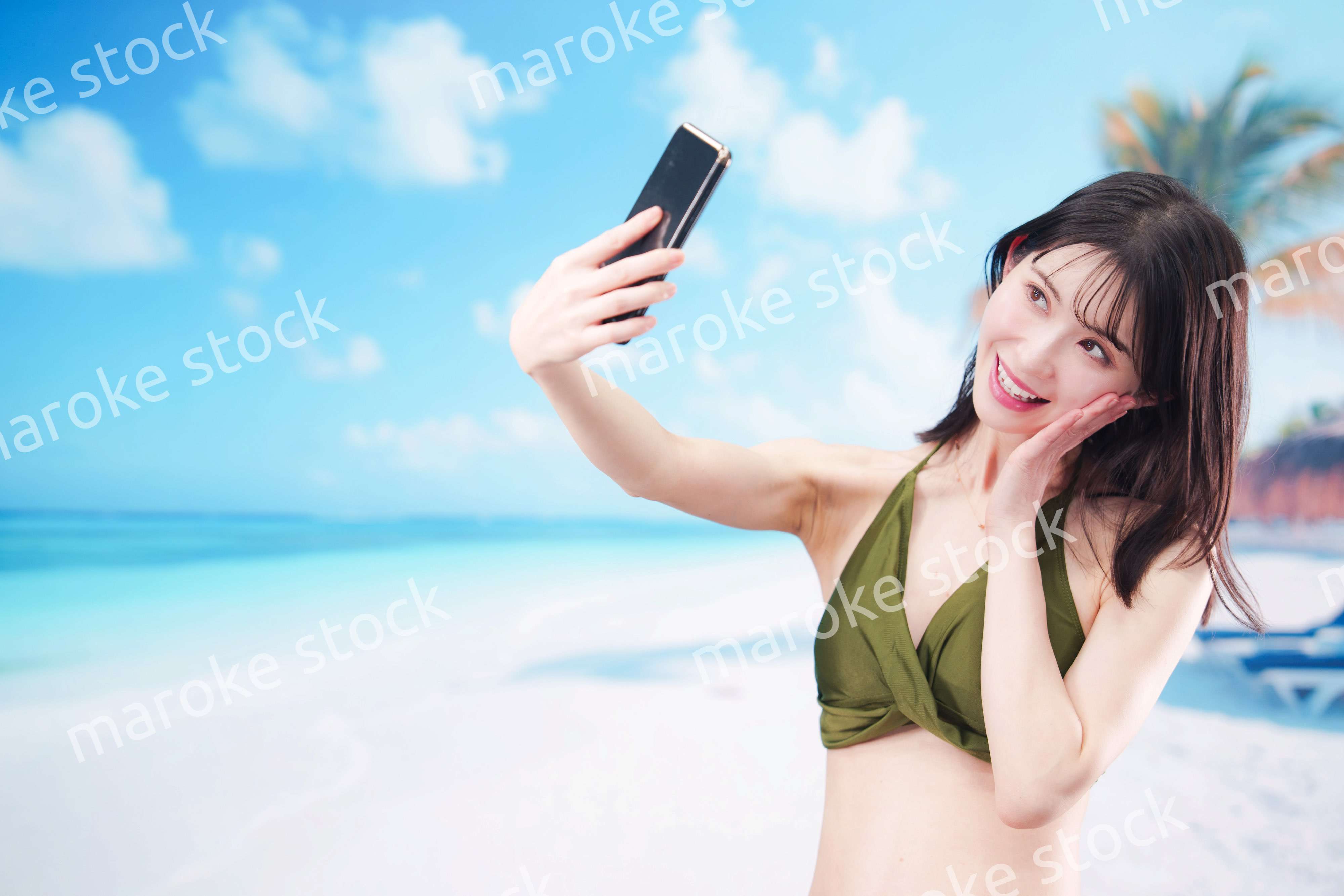 快晴のビーチでスマホで自撮りをする水着を着た若い女性
