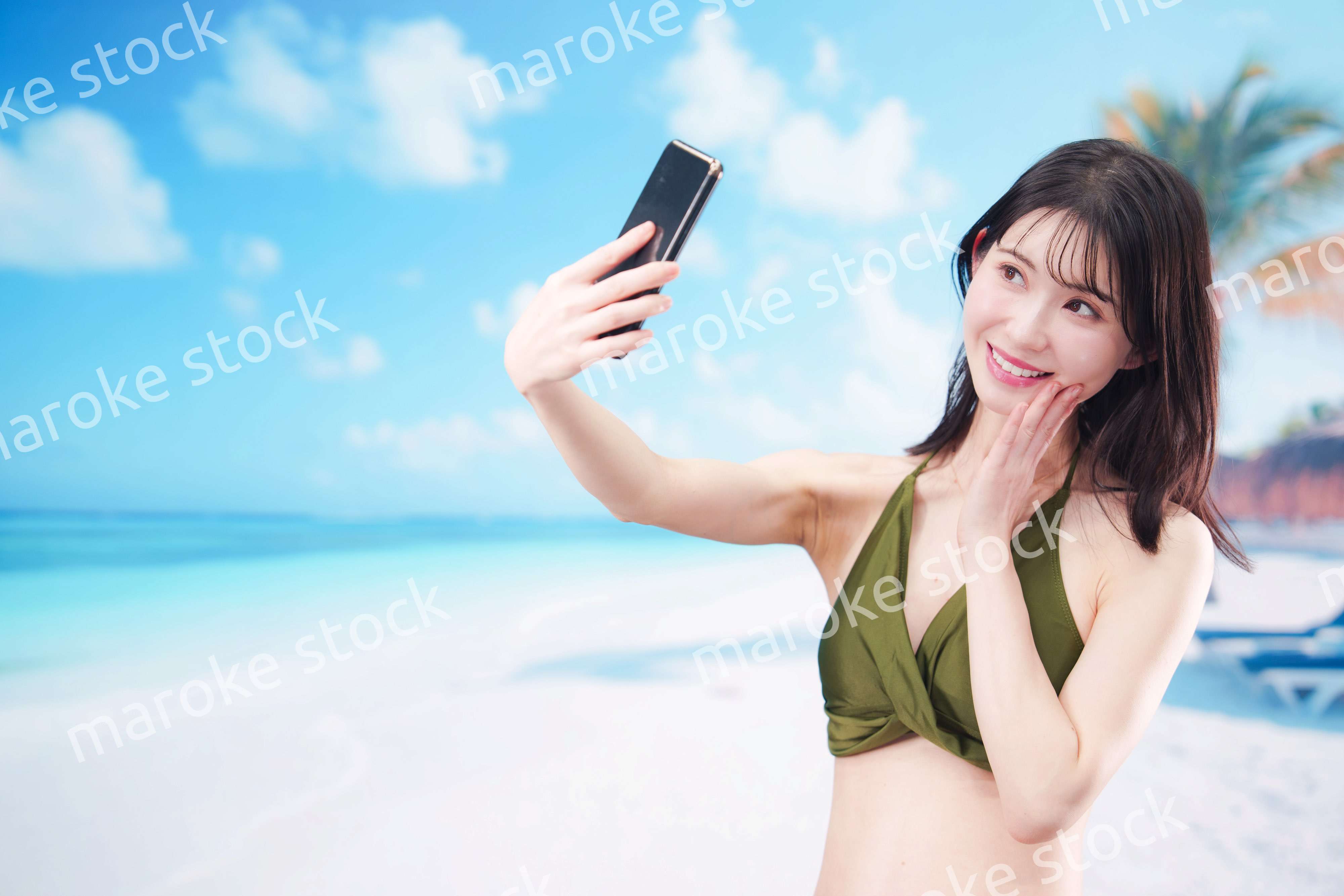 快晴のビーチでスマホで自撮りをする水着を着た若い女性