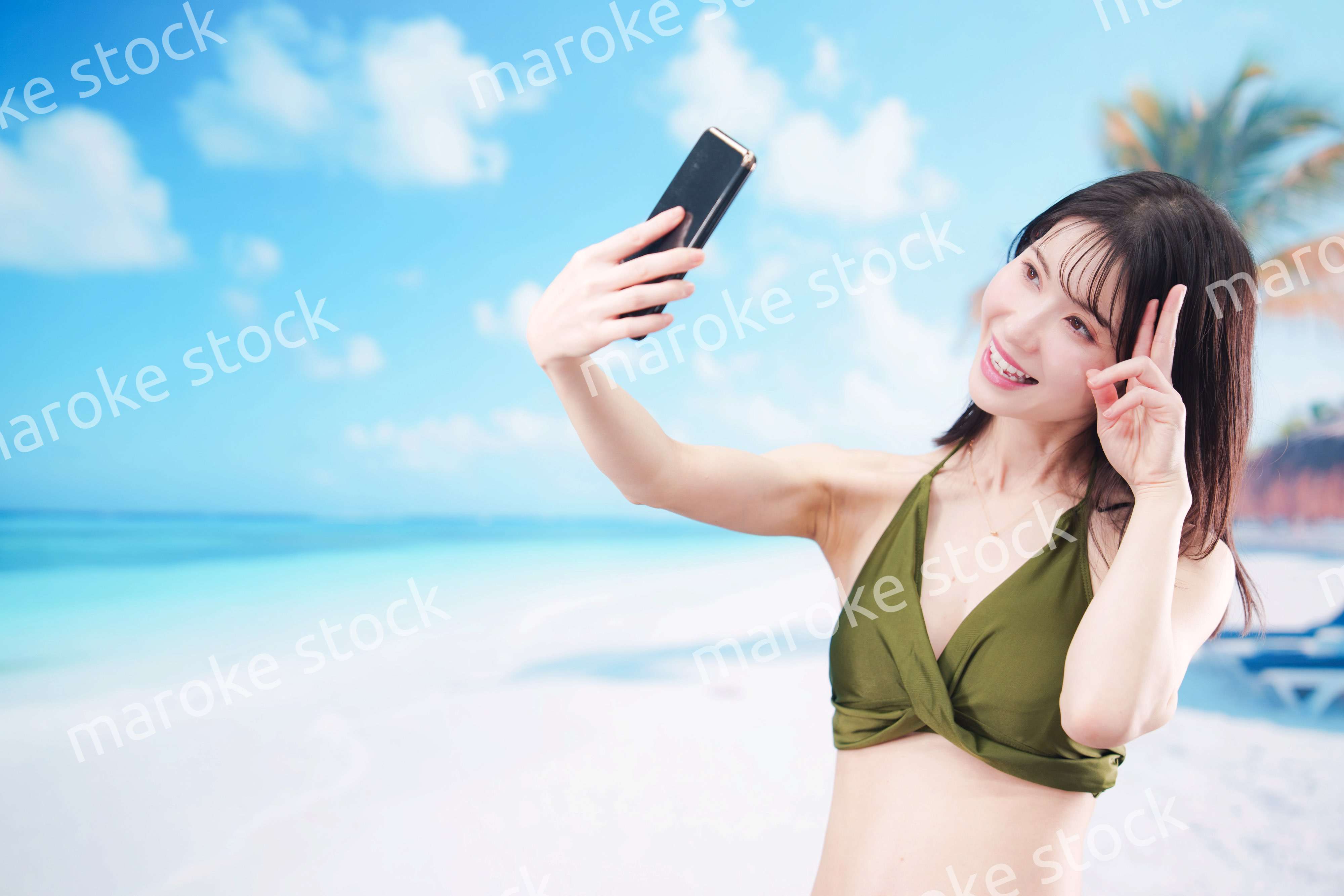 快晴のビーチでスマホで自撮りをする水着を着た若い女性