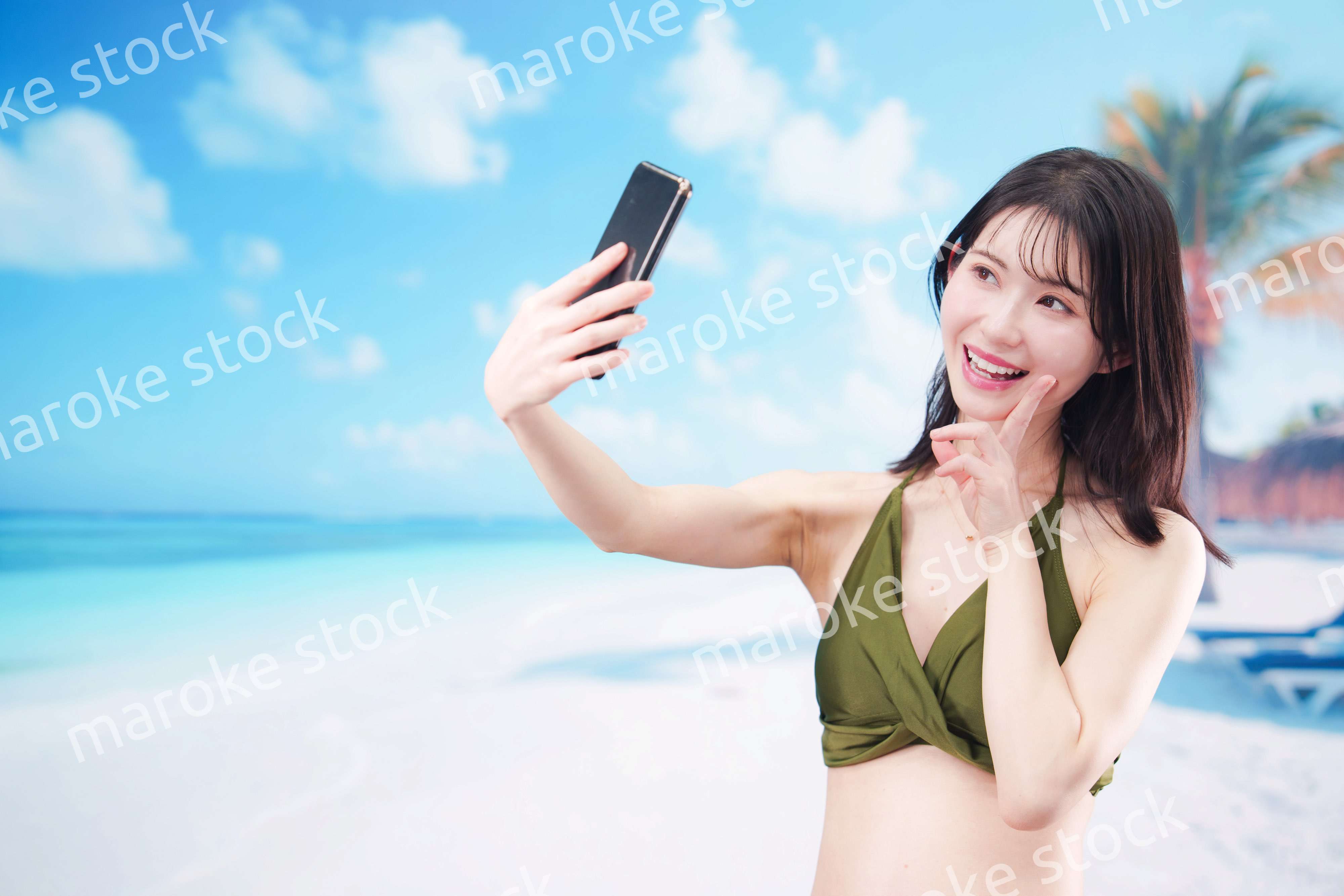 快晴のビーチでスマホで自撮りをする水着を着た若い女性