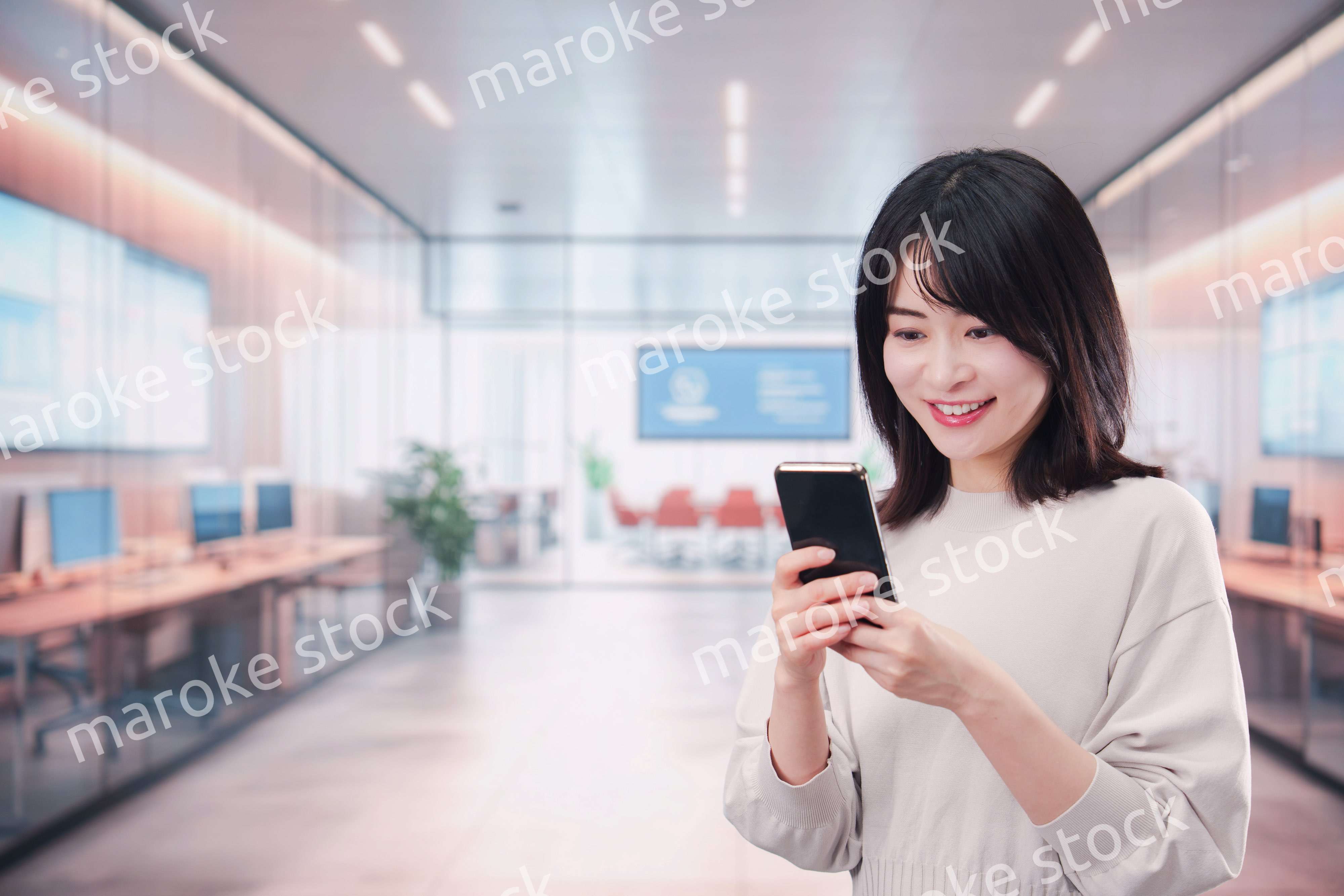 明るいオフィスでスマホを使う若い女性