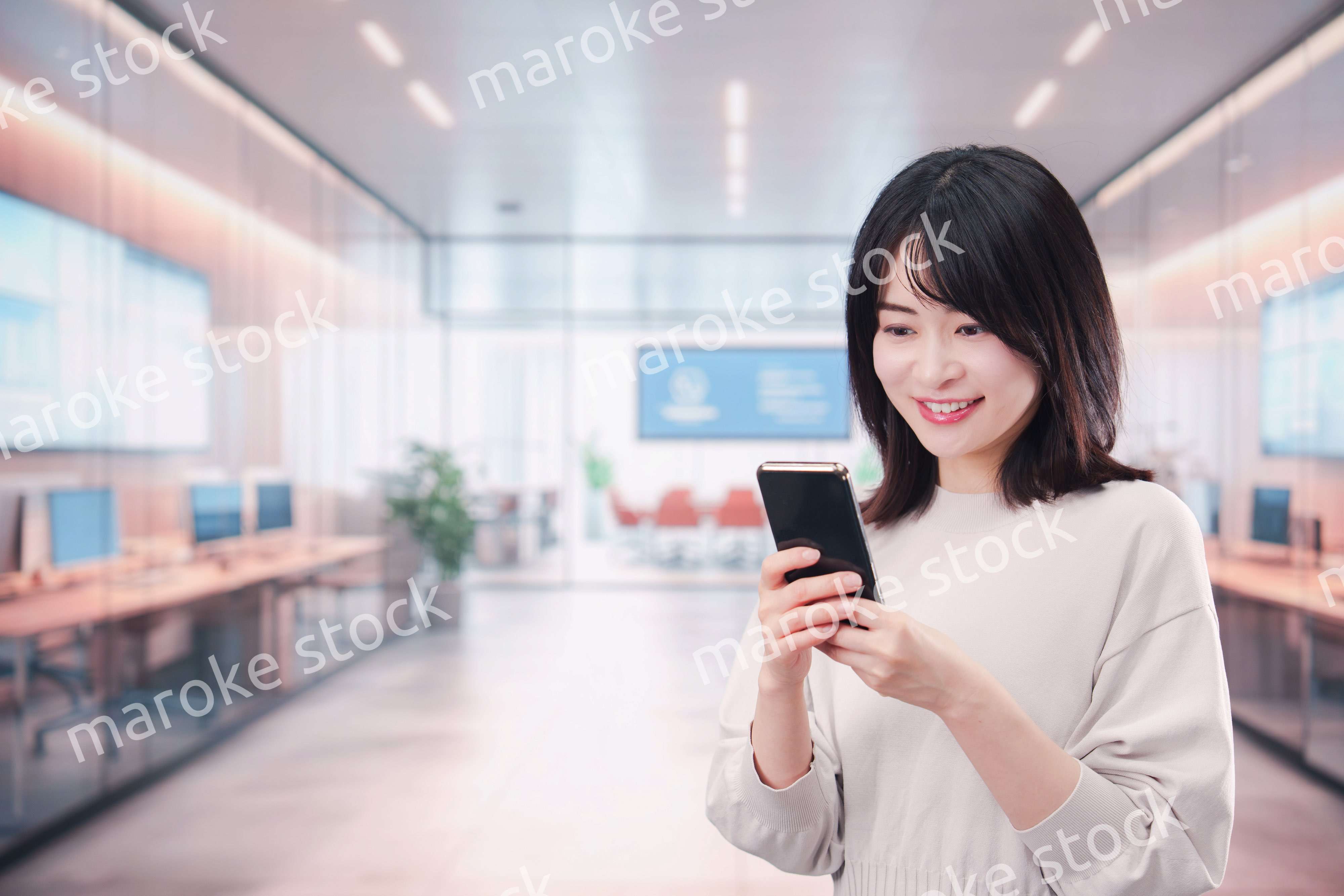 明るいオフィスでスマホを使う若い女性