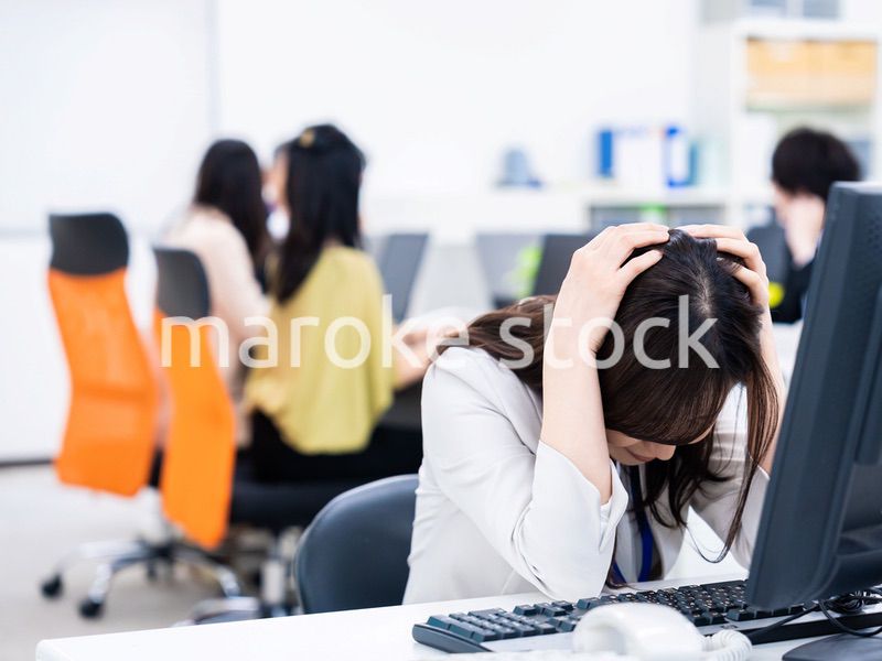 デスクワークをしながら頭を抱えるビジネスウーマン