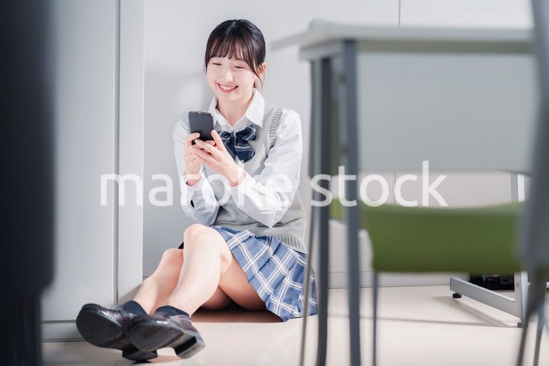 教室で笑顔でスマホを使う女子高生