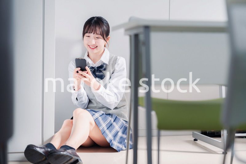 教室で笑顔でスマホを使う女子高生