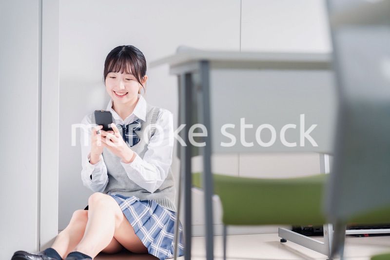 教室で笑顔でスマホを使う女子高生