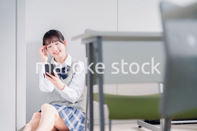 教室で笑顔でスマホを使う女子高生