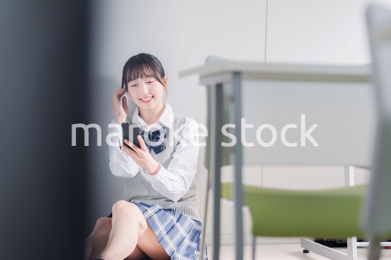 教室で笑顔でスマホを使う女子高生