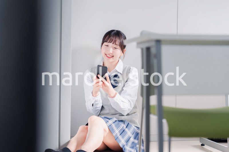 教室で笑顔でスマホを使う女子高生