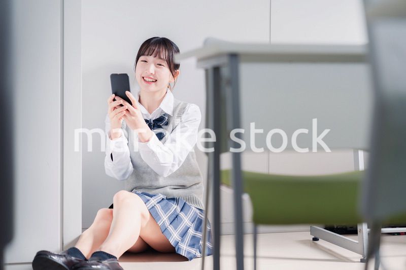 教室で笑顔でスマホを使う女子高生
