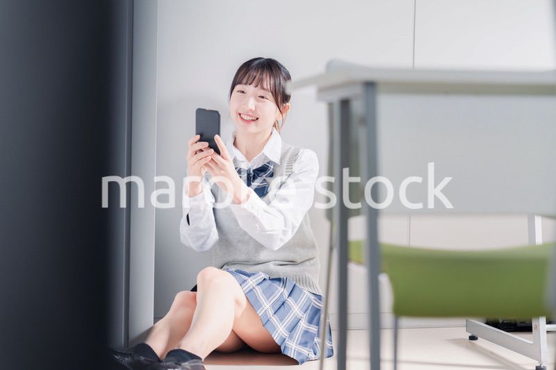 教室で笑顔でスマホを使う女子高生