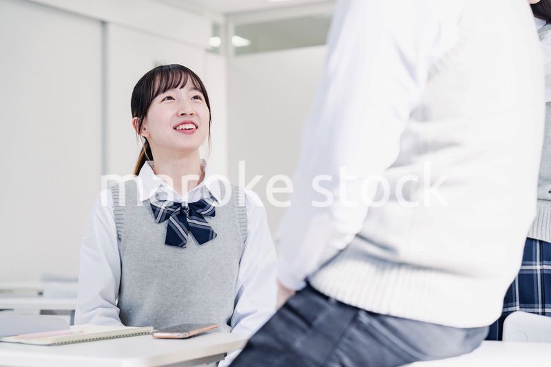 教室でクラスメイトと雑談をする高校生