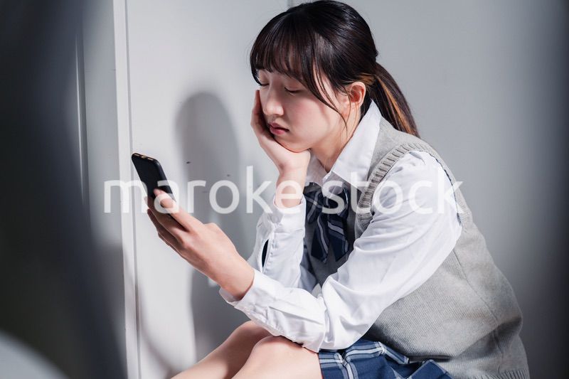スマホを見ながら落ち込む女子高生
