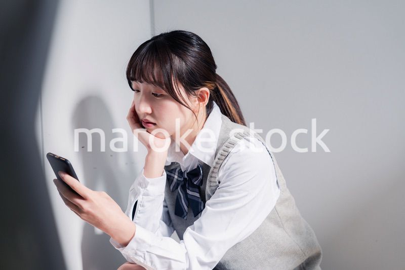 スマホを見ながら落ち込む女子高生