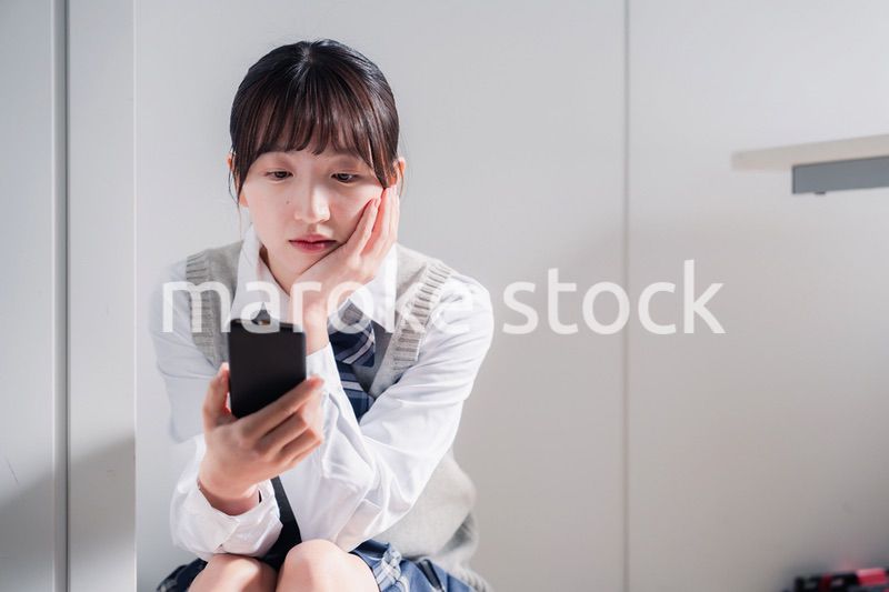 スマホを見ながら落ち込む女子高生