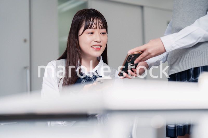 教室でスマホを見ながら話す女子高生