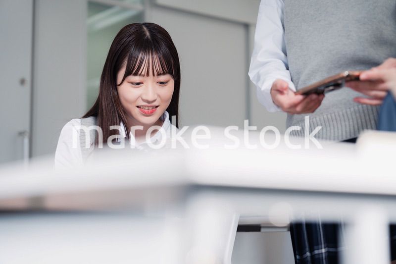 教室でスマホを見ながら話す女子高生
