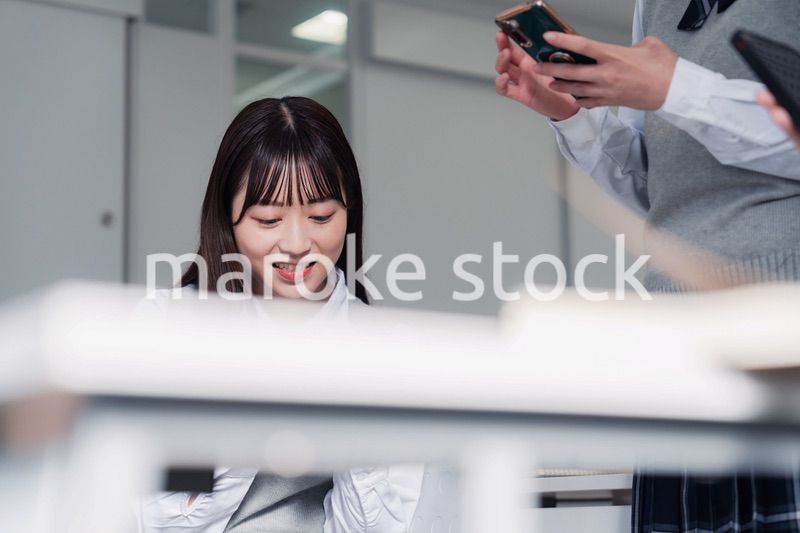 教室でスマホを見ながら話す女子高生