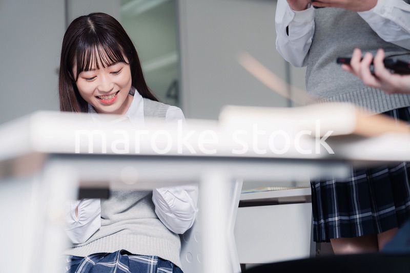 教室でスマホを見ながら話す女子高生