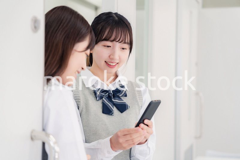 教室でスマホを見ながら話す女子高生