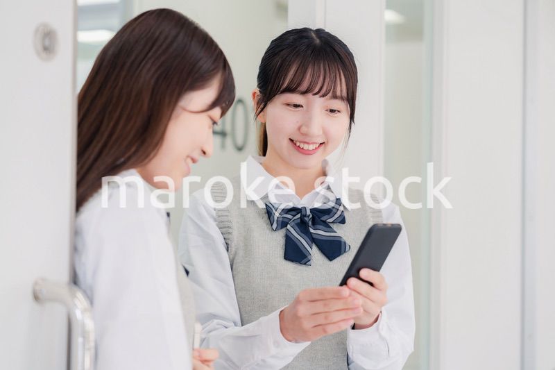 教室でスマホを見ながら話す女子高生