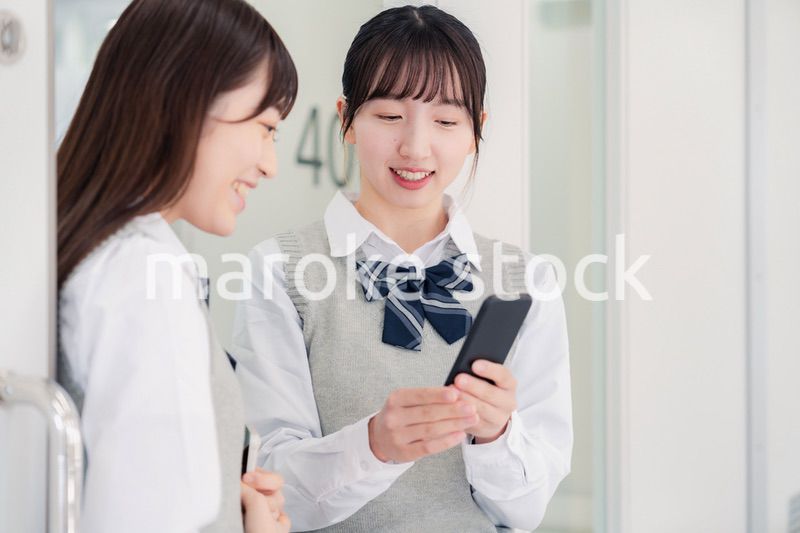 教室でスマホを見ながら話す女子高生
